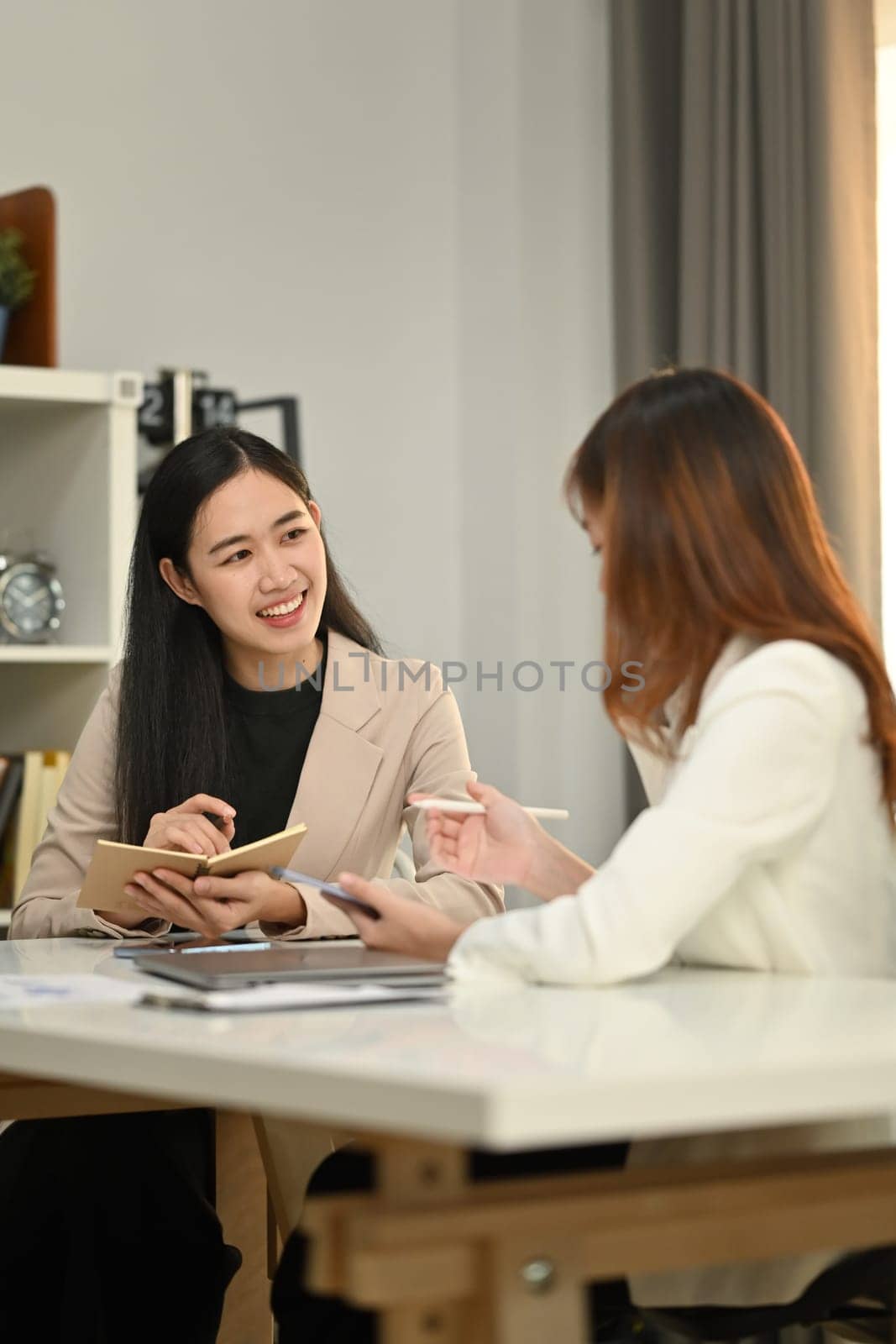 Smiling asian female manager explaining information on digital tablet to colleague in modern corporate office.