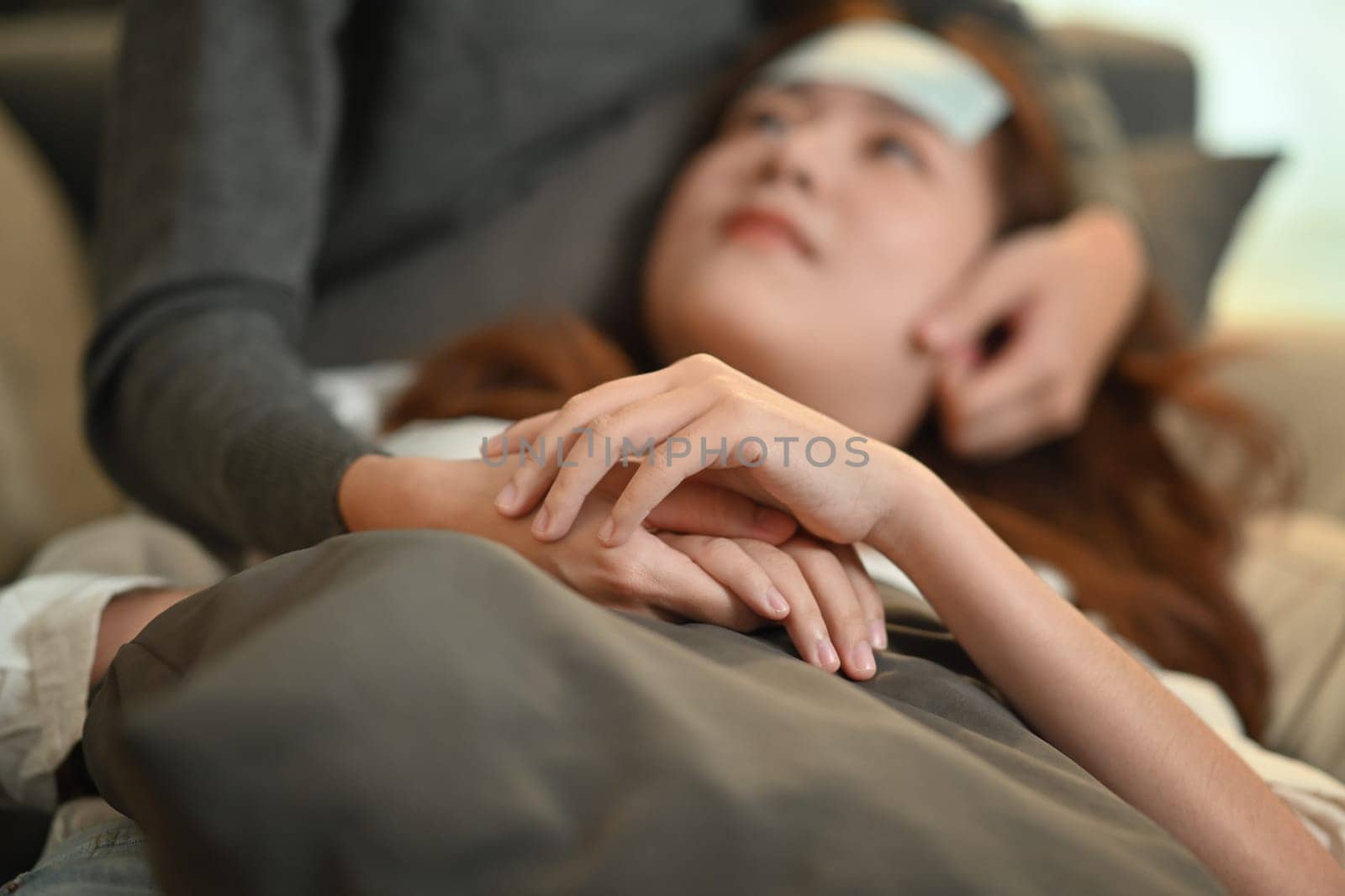 Sick young women with fever lying on couch while loving girlfriend taking care of her. LGBT, equal rights and love concept by prathanchorruangsak
