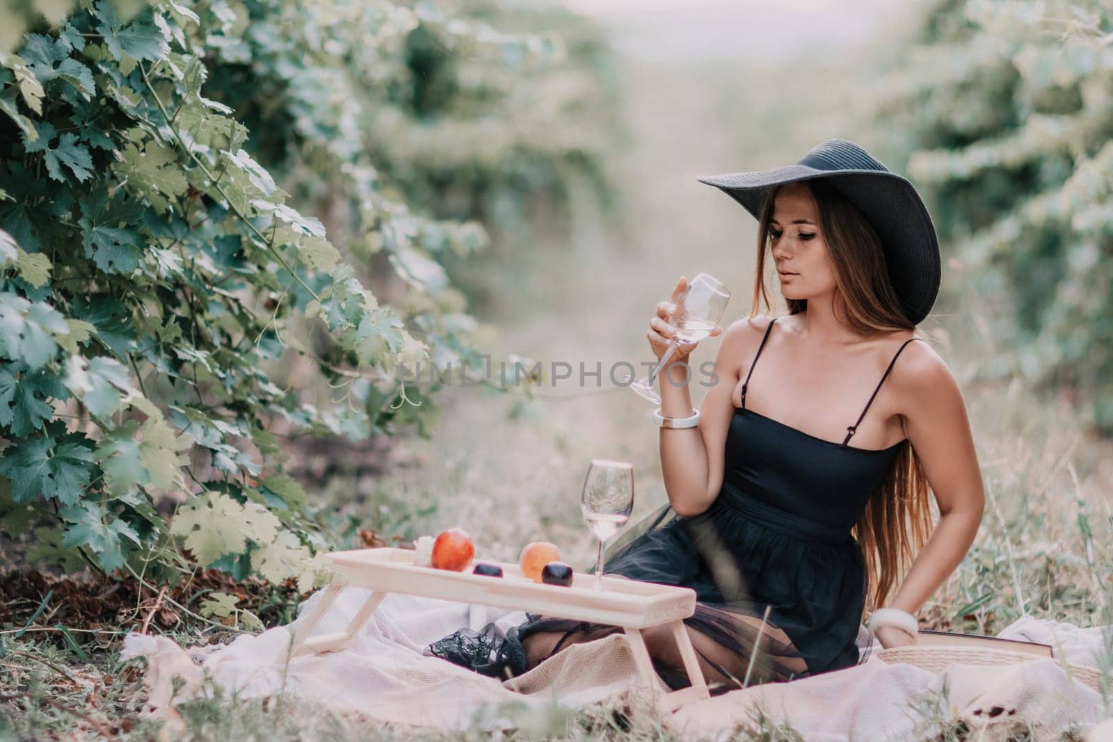 Woman picnic vineyard. Happy woman with a glass of wine at a picnic in the vineyard, wine tasting at sunset and open nature in the summer. Romantic dinner, fruit and wine. by panophotograph