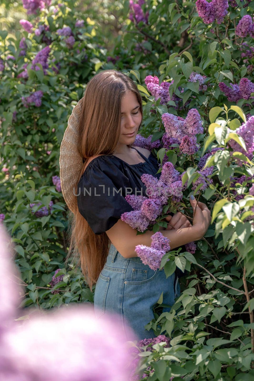 portrait of young woman with long hair outdoors in blooming lilac garden.