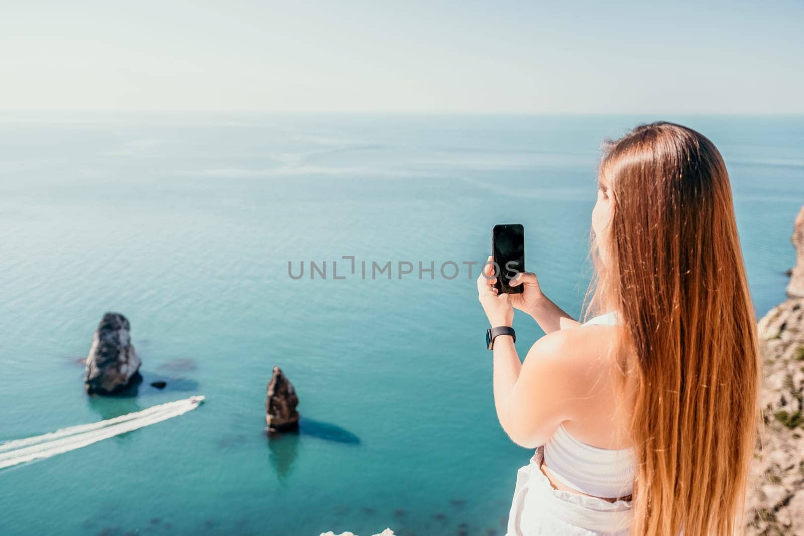 Digital nomad, woman in the hat, a business woman with a laptop sits on the rocks by the sea during sunset, makes a business transaction online from a distance. Freelance, remote work on vacation. by panophotograph