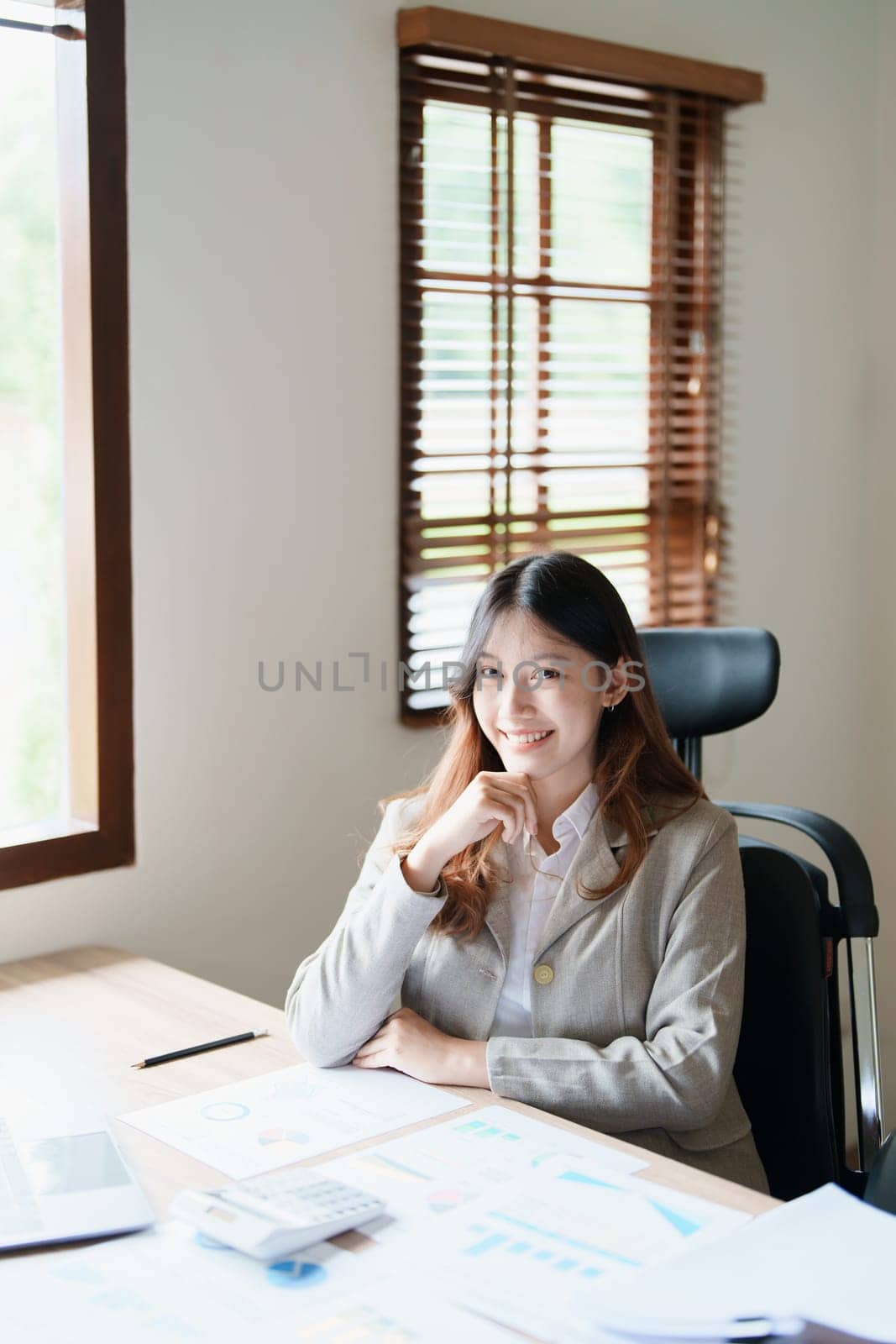 Portrait of a woman business owner showing a happy smiling face as he has successfully invested her business using computers and financial budget documents at work.