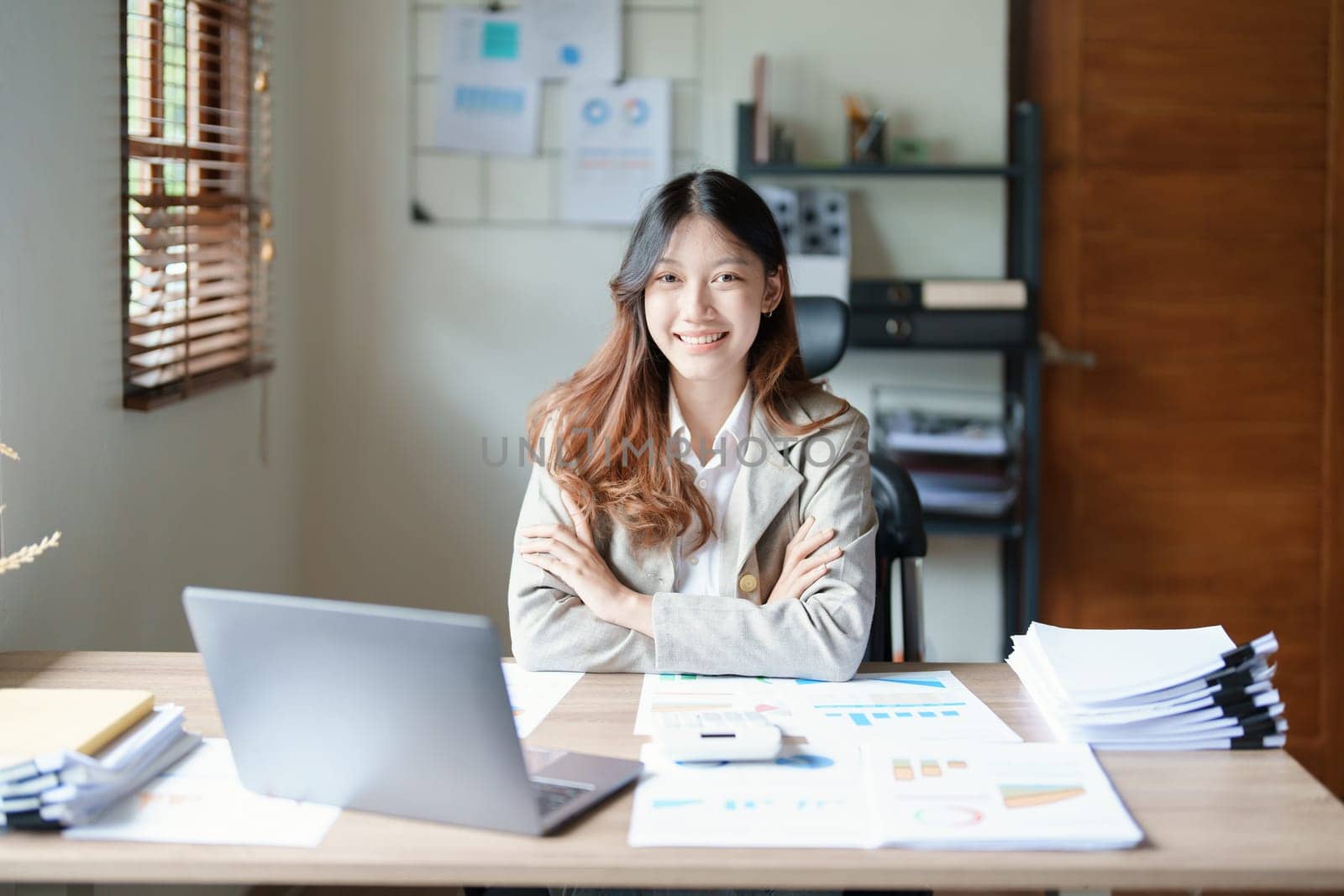 Portrait of a woman business owner showing a happy smiling face as he has successfully invested her business using computers and financial budget documents at work.