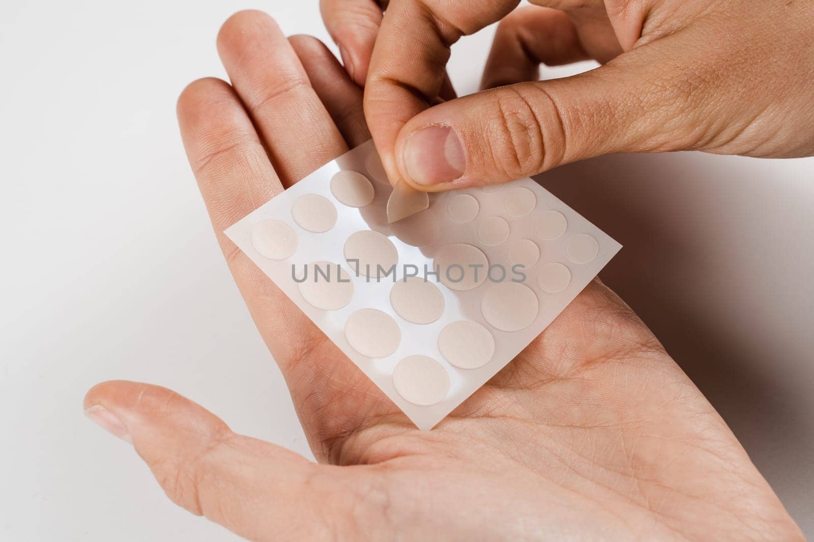 Girl taking acne patch for treatment of pimple and rosacea close-up. Facial rejuvenation cleansing cosmetology. Set of round patches for acne in hands on white background. by Rabizo