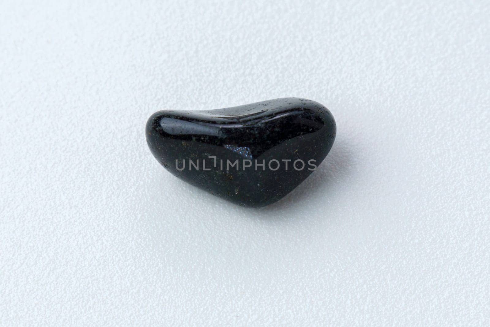 Close up of natural mineral from geological collection tumbled black onyx gem stone, white background