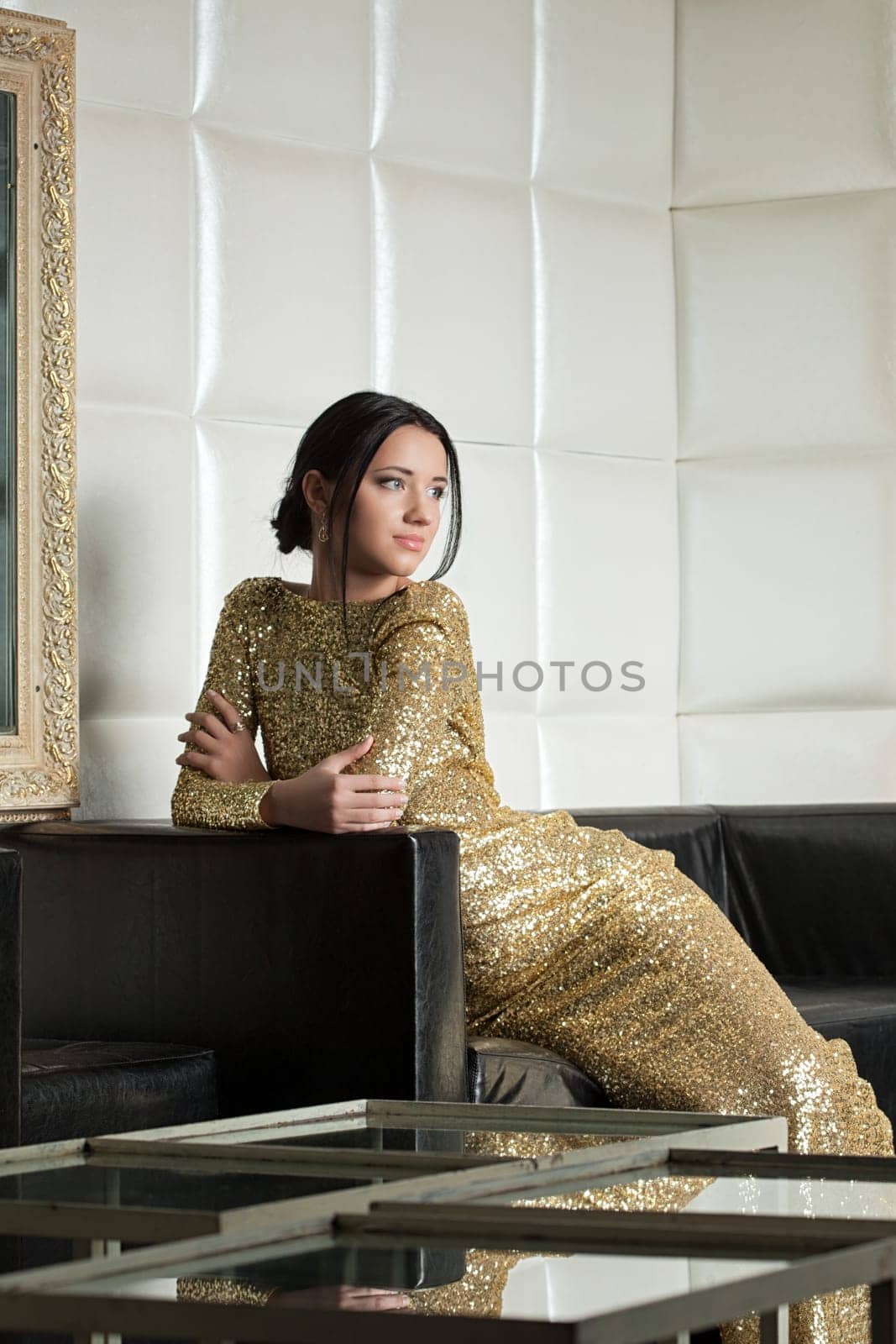 Portrait of brunette woman in gold dress posing on sofa
