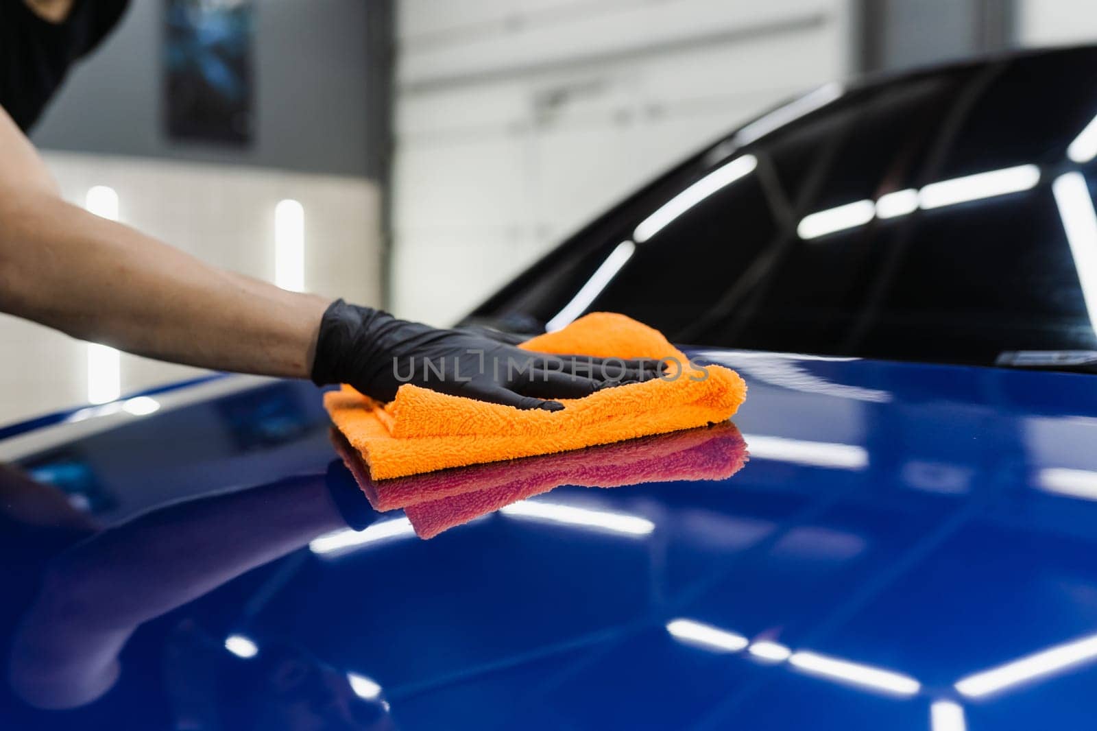 Hand car drying with microfiber in detailing auto service. Cleaner worker dry body car after washing automobile
