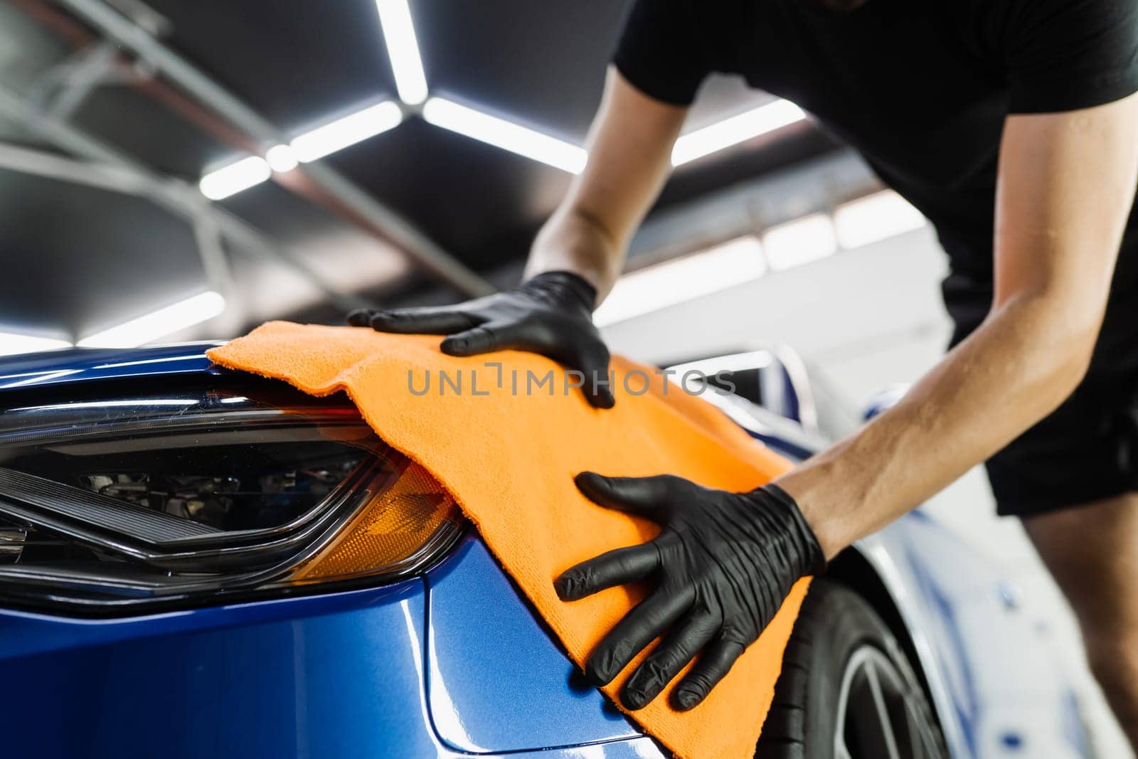 Hand car drying with microfiber in detailing auto service. Cleaner worker dry body car after washing automobile