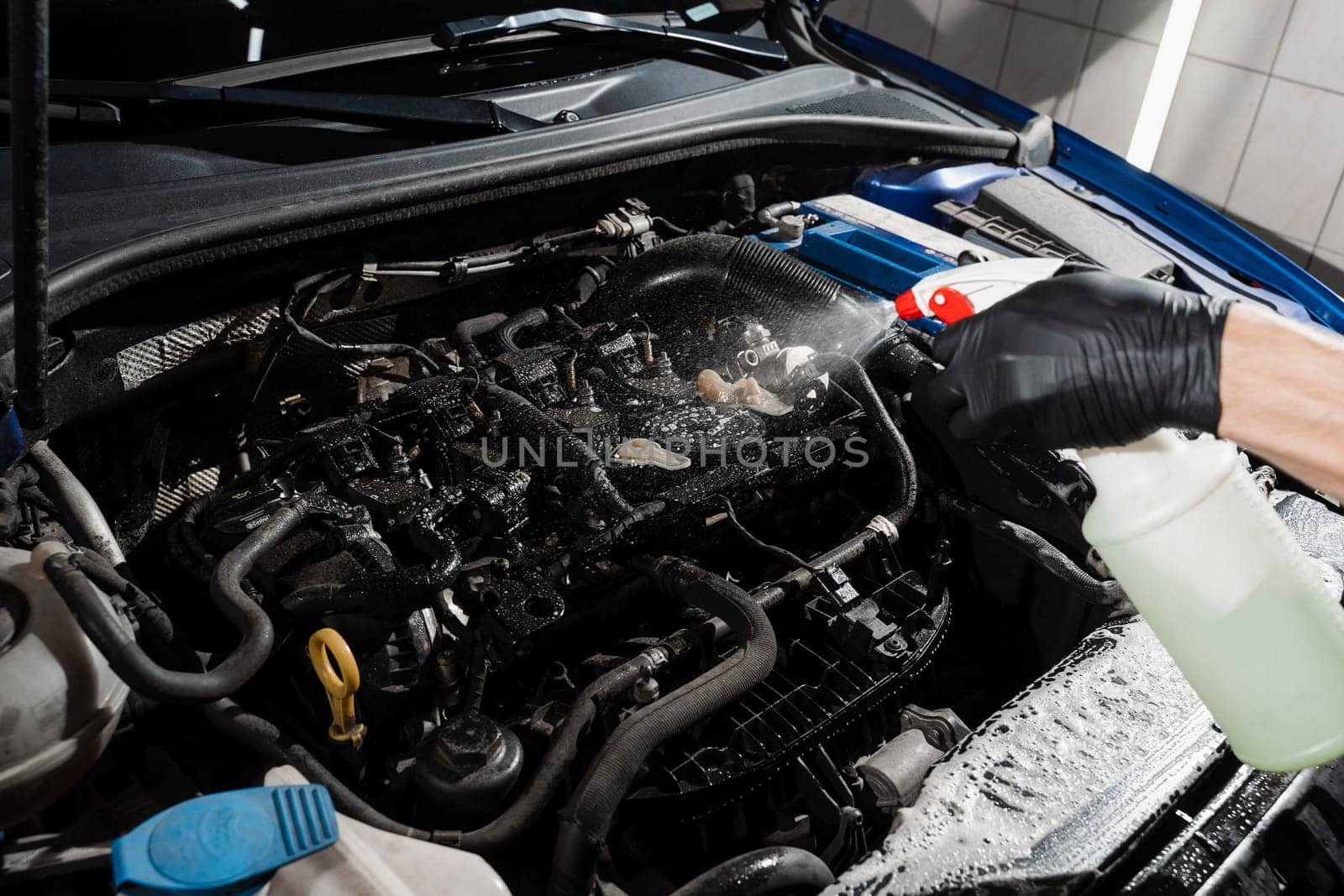 Spraying detergent on car engine. Washing car engine with spray and detergent in detailing auto service. Detailing cleaning motor from dust and dirt