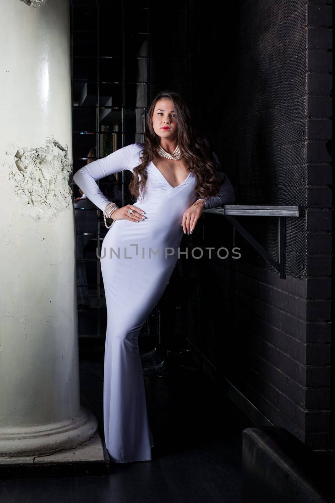 Luxurious brunette posing in elegant white dress near column