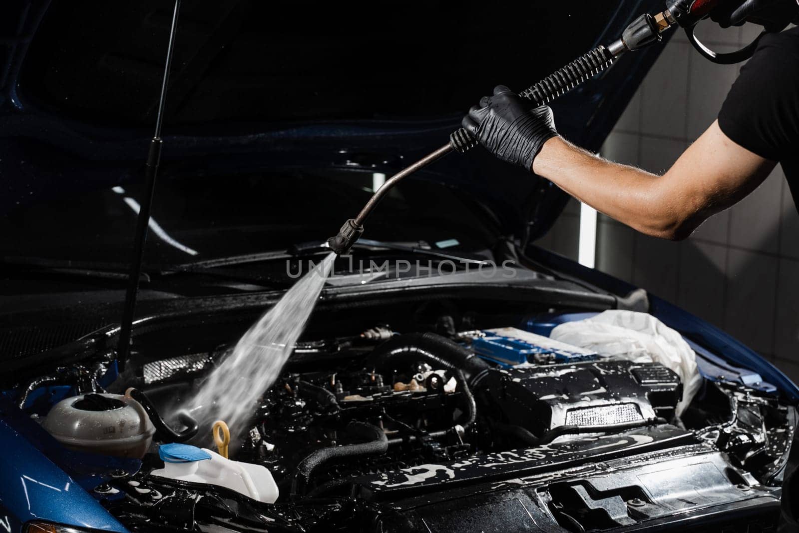 Pouring water on car engine. Washing car engine with spray, brush and detergent in detailing auto service. Detailing cleaning motor from dust and dirt