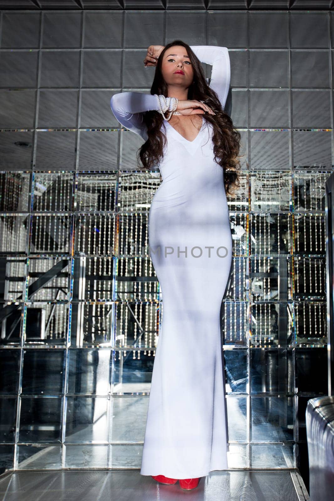 Elegant young woman posing in long white dress on mirror background