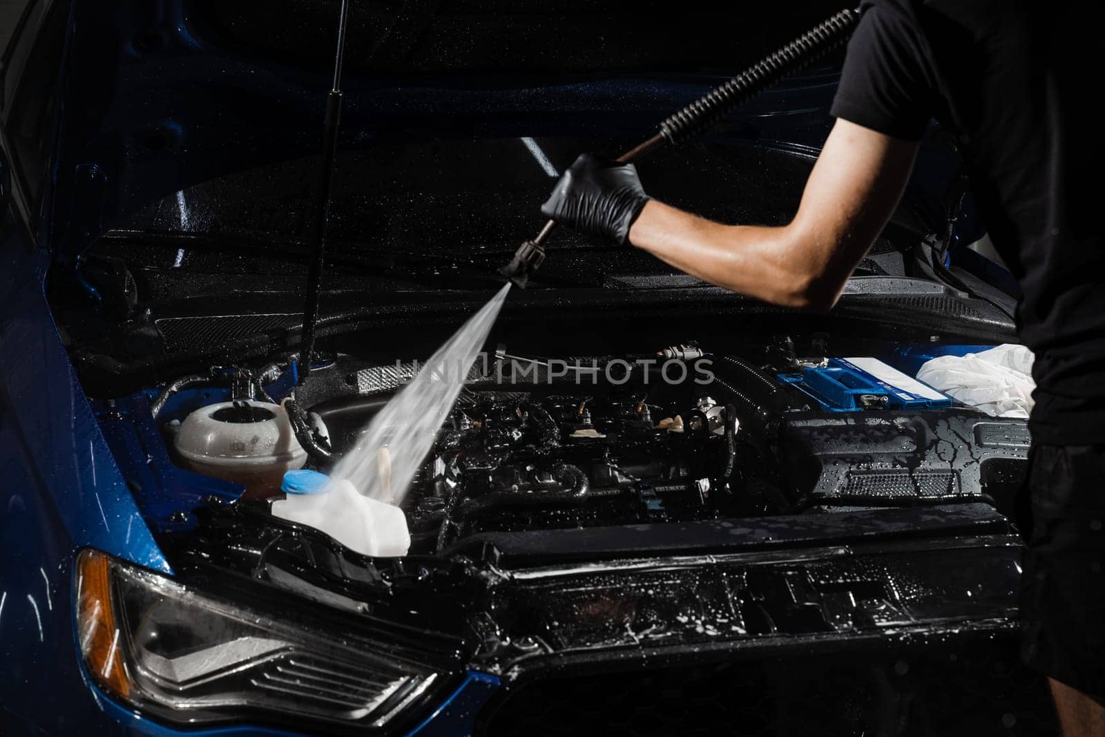 Pouring water on car engine. Washing car engine with spray, brush and detergent in detailing auto service. Detailing cleaning motor from dust and dirt. by Rabizo