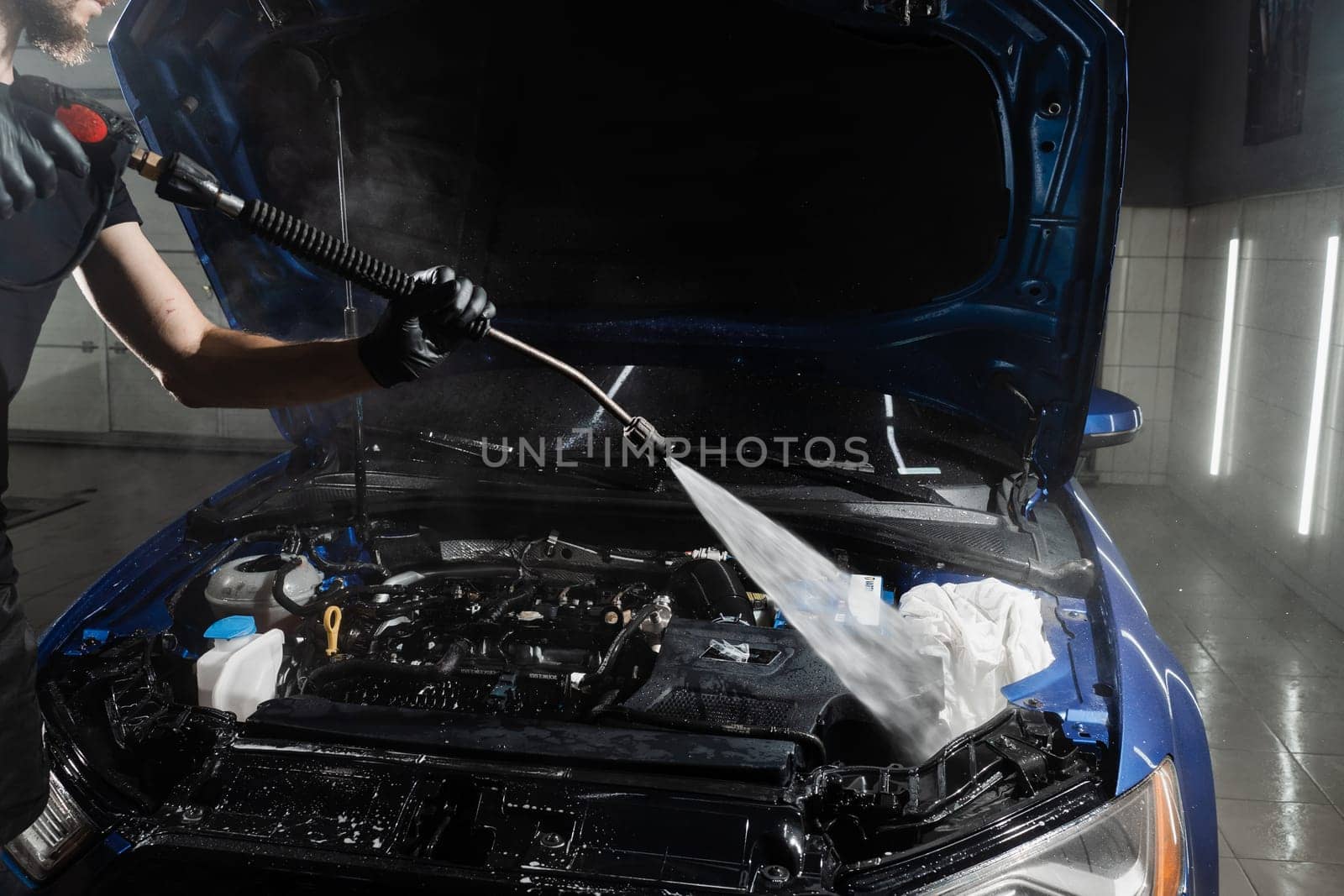 Washing car engine with with water in detailing auto service. Detailing cleaning motor from dust and dirt. Pouring water on car engine