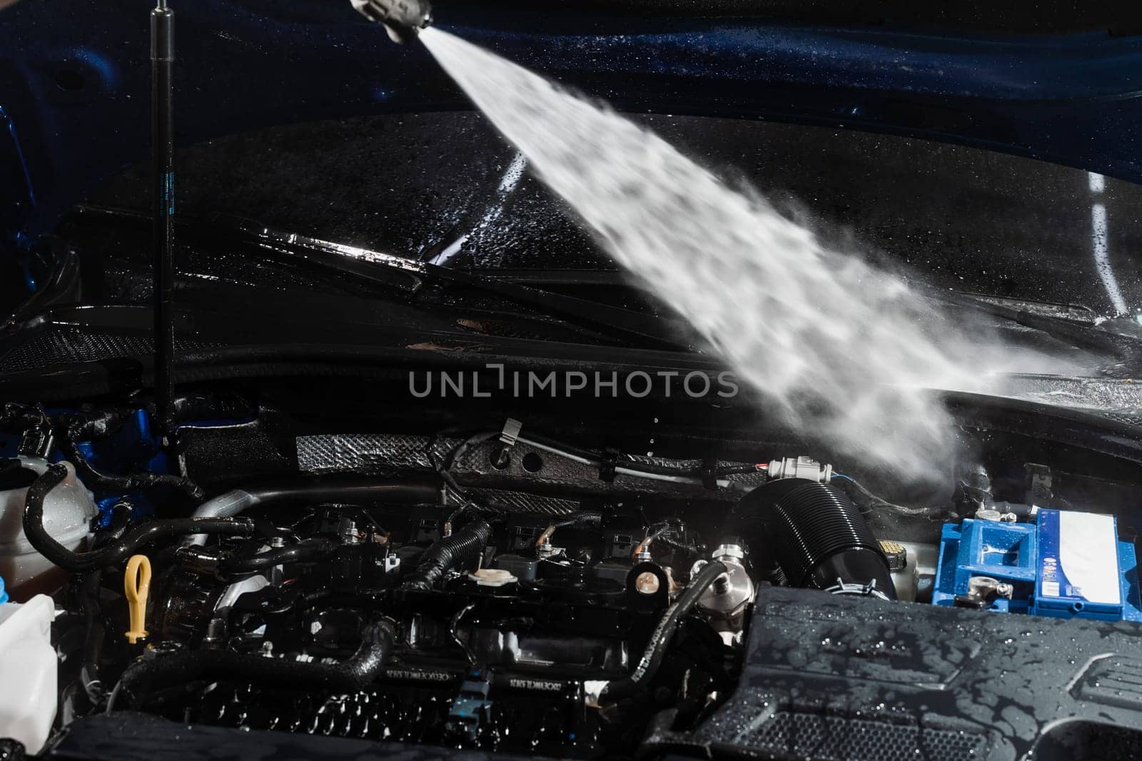 Washing car engine with with water in detailing auto service. Detailing cleaning motor from dust and dirt. Pouring water on car engine