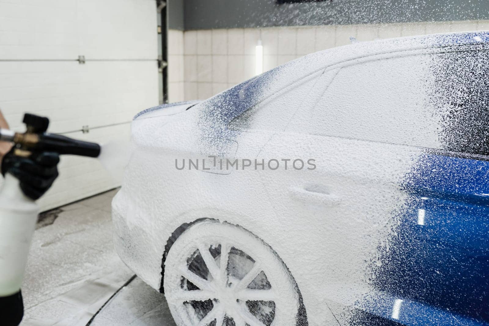 Process of spraying foam on the car body in the garage. Second phase of detailing washing in car service. Car washer does full body car wash