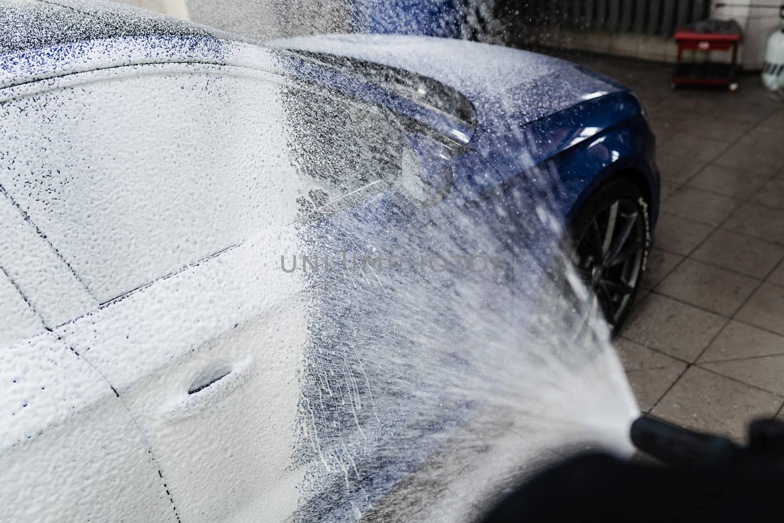 Car washer does full body car wash. Process of spraying foam on the car body in the garage. Second phase of detailing washing in car service