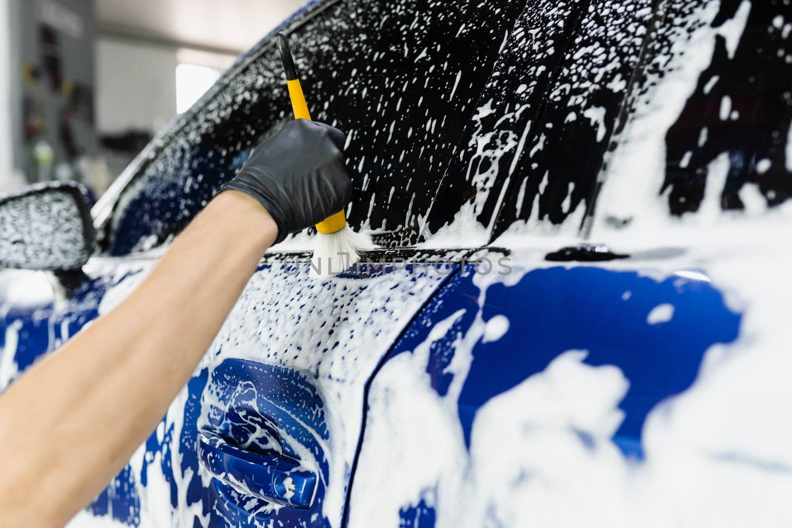 Hand brush washing of car body with foam in car detailing service. Car wash worker washes a car body