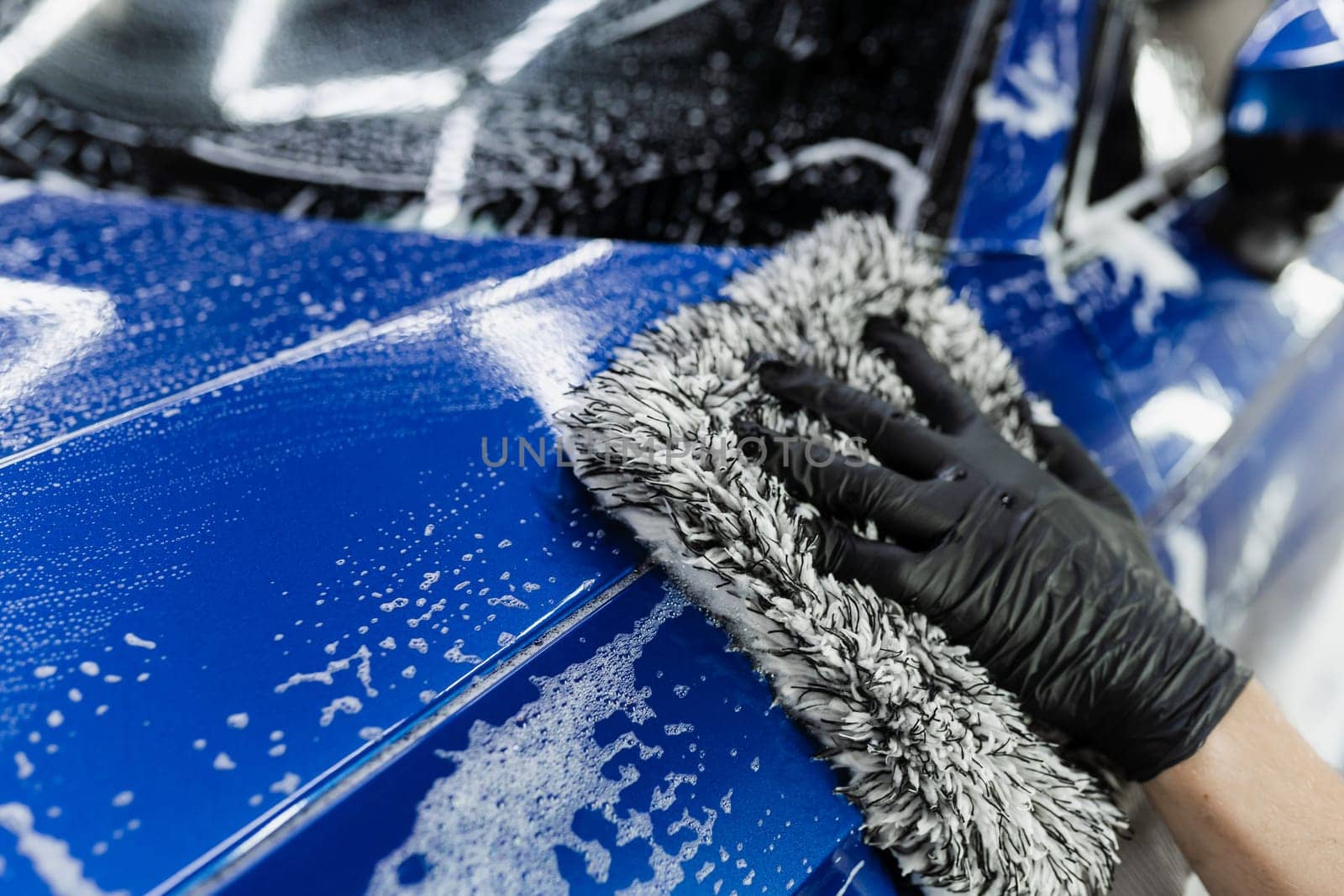 Hand washing with microfiber glove with foam car body in garage. Car washer doing manual foam washing in auto detailing service