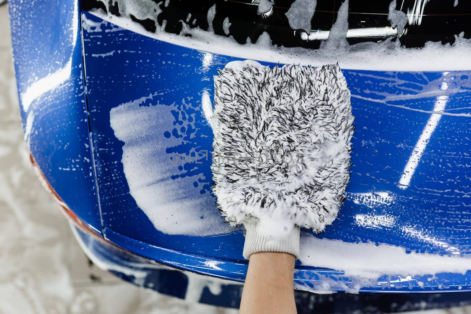 Car washer doing manual foam washing in auto detailing service. Hand washing with microfiber glove with foam car body in garage. by Rabizo