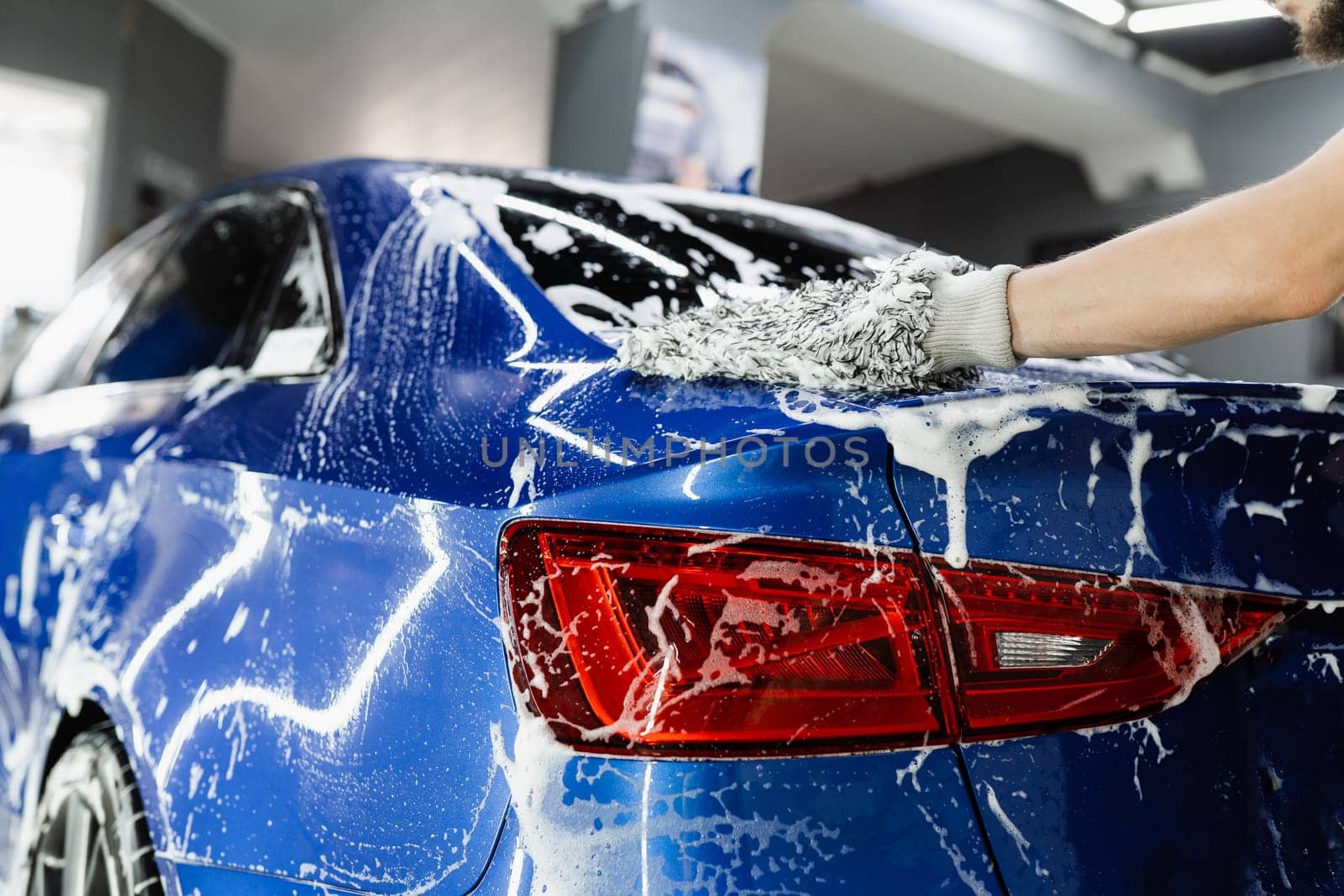 Hand washing with microfiber glove with foam car body in garage. Car washer doing manual foam washing in auto detailing service