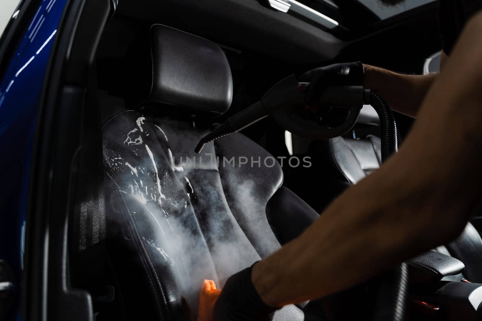 Steam cleaning of leather seat after foam and detergent washing. Worker in auto cleaning service clean car inside. Car interior detailing