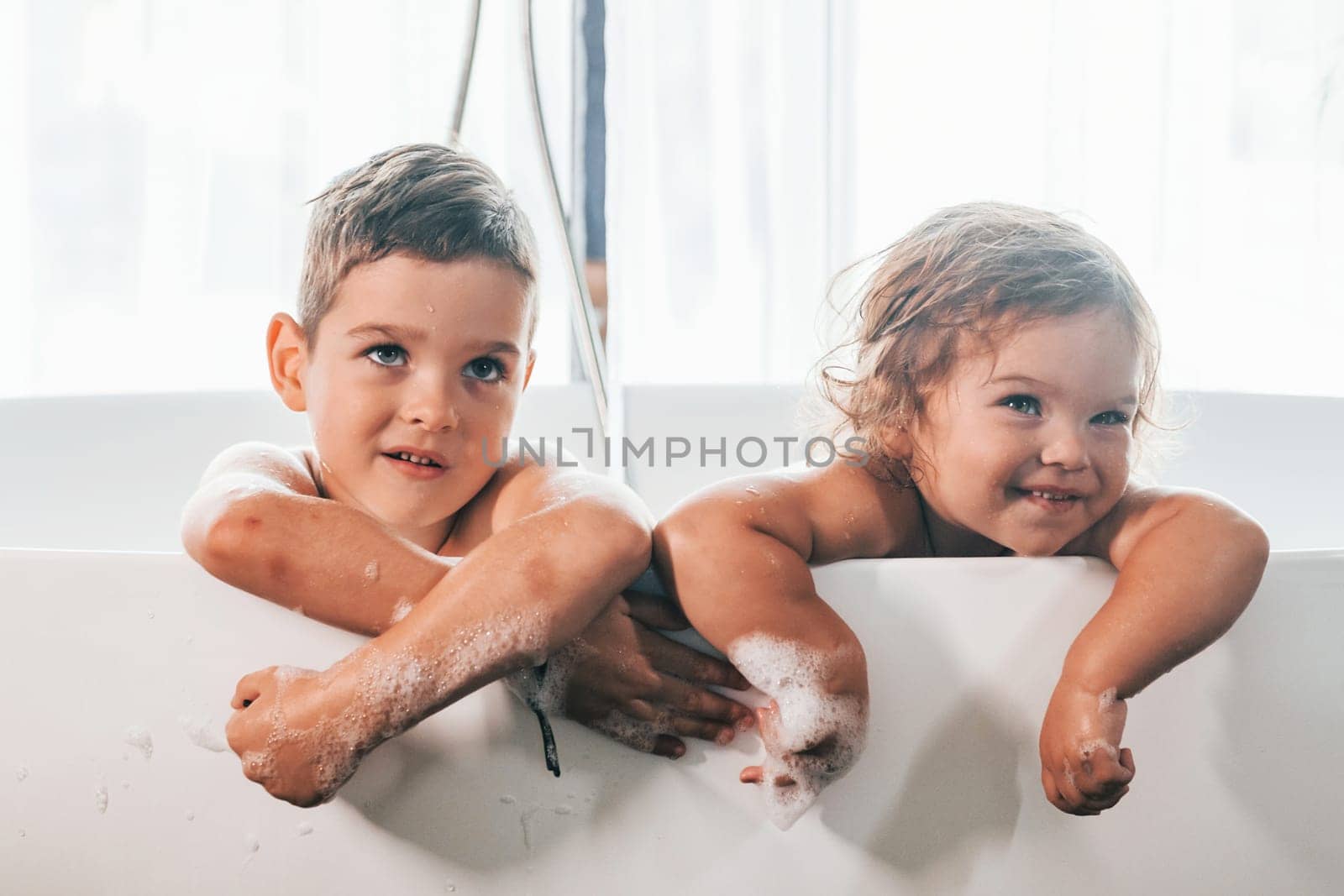 Two kids having fun and washing themselves in the bath at home. Posing for a camera by Standret
