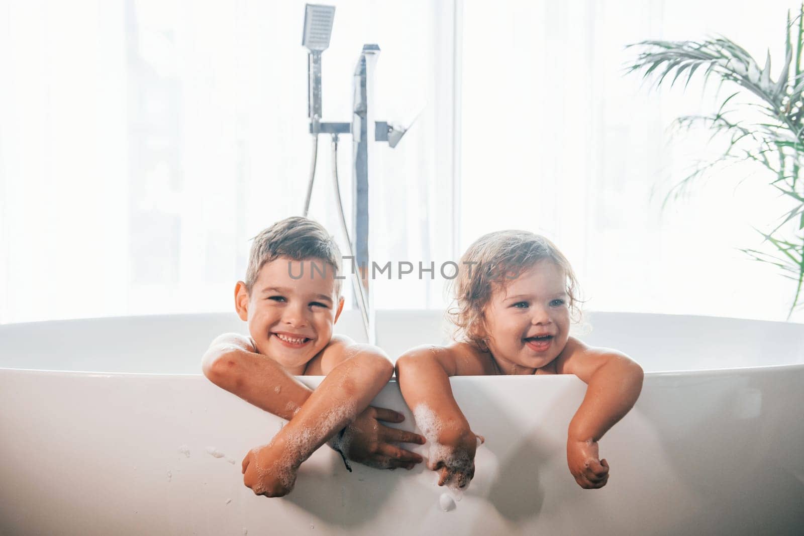 Two kids having fun and washing themselves in the bath at home. Posing for a camera by Standret