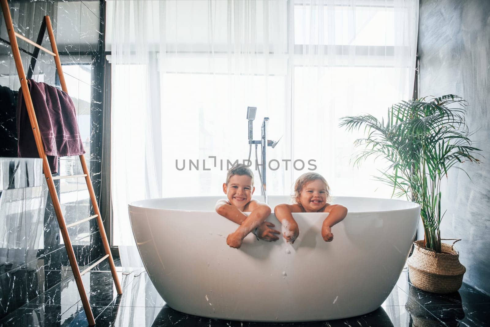 Two kids having fun and washing themselves in the bath at home. Posing for a camera by Standret