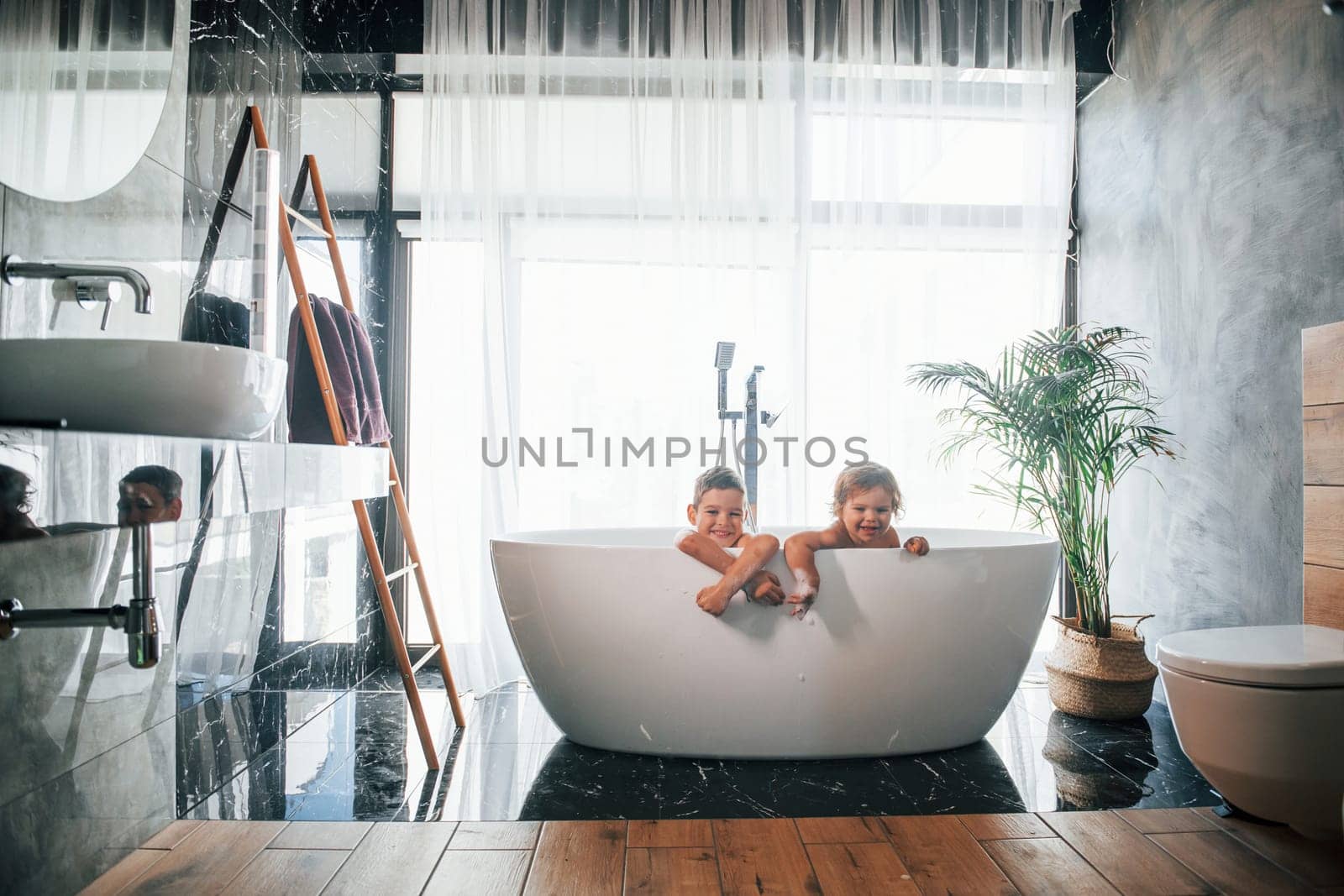 Two kids having fun and washing themselves in the bath at home. Posing for a camera by Standret