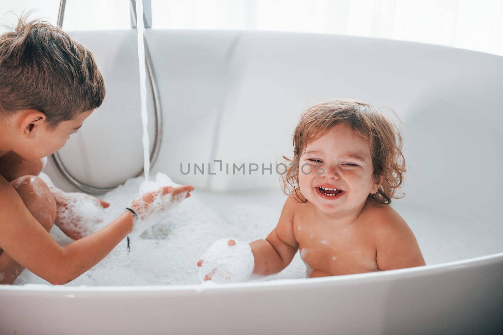 Two kids having fun and washing themselves in the bath at home. Posing for a camera by Standret