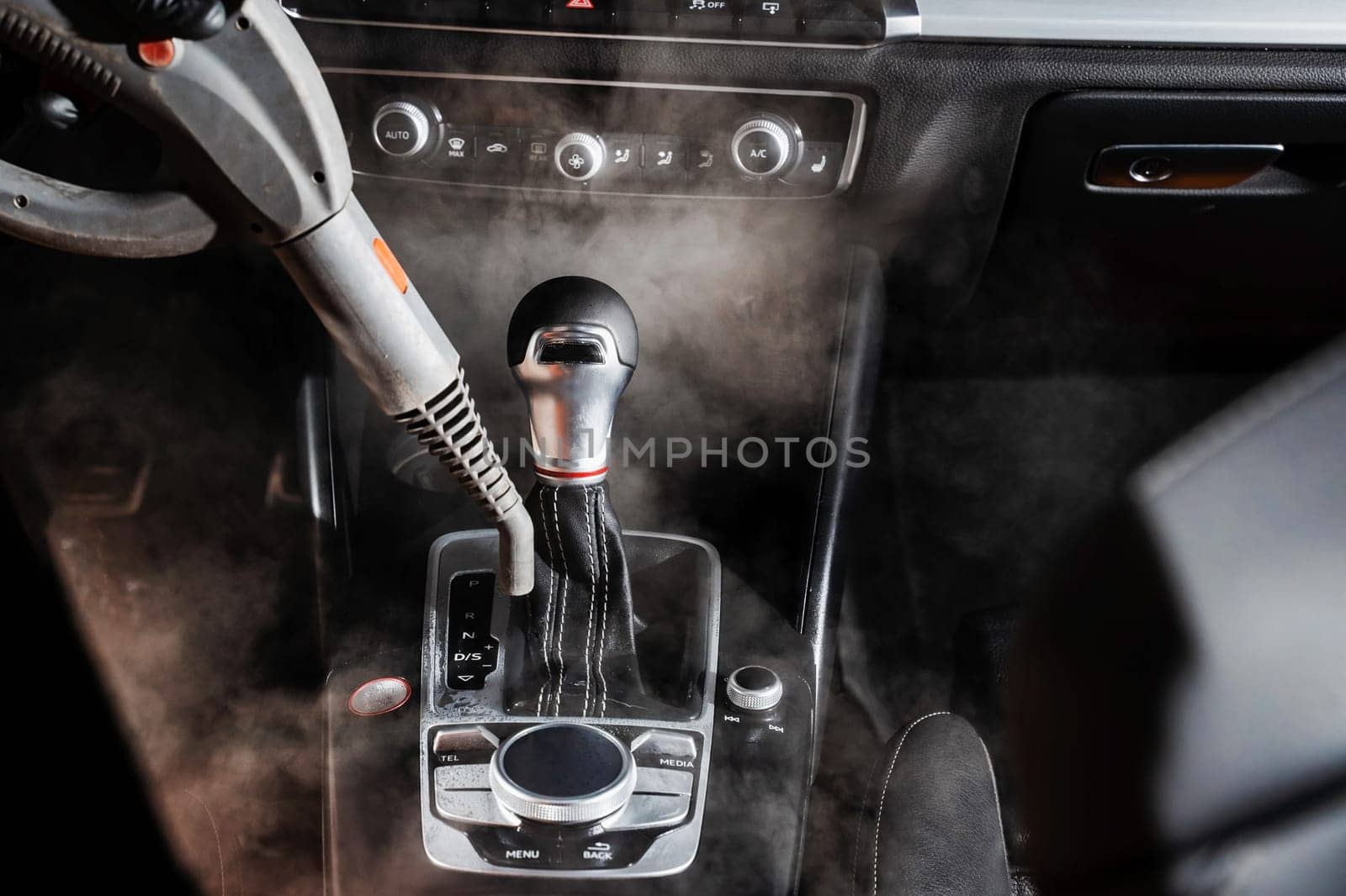 Steam cleaning of gearbox and dashboard in car. Vaping steam. Cleaning individual elements of black leather interior in auto. Creative advert for auto detailing service