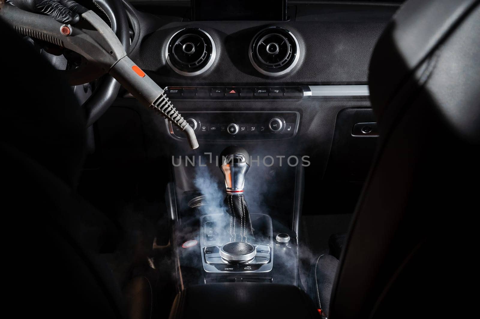 Steam cleaning of gearbox and dashboard in car. Vaping steam. Cleaning individual elements of black leather interior in auto. Creative advert for auto detailing service