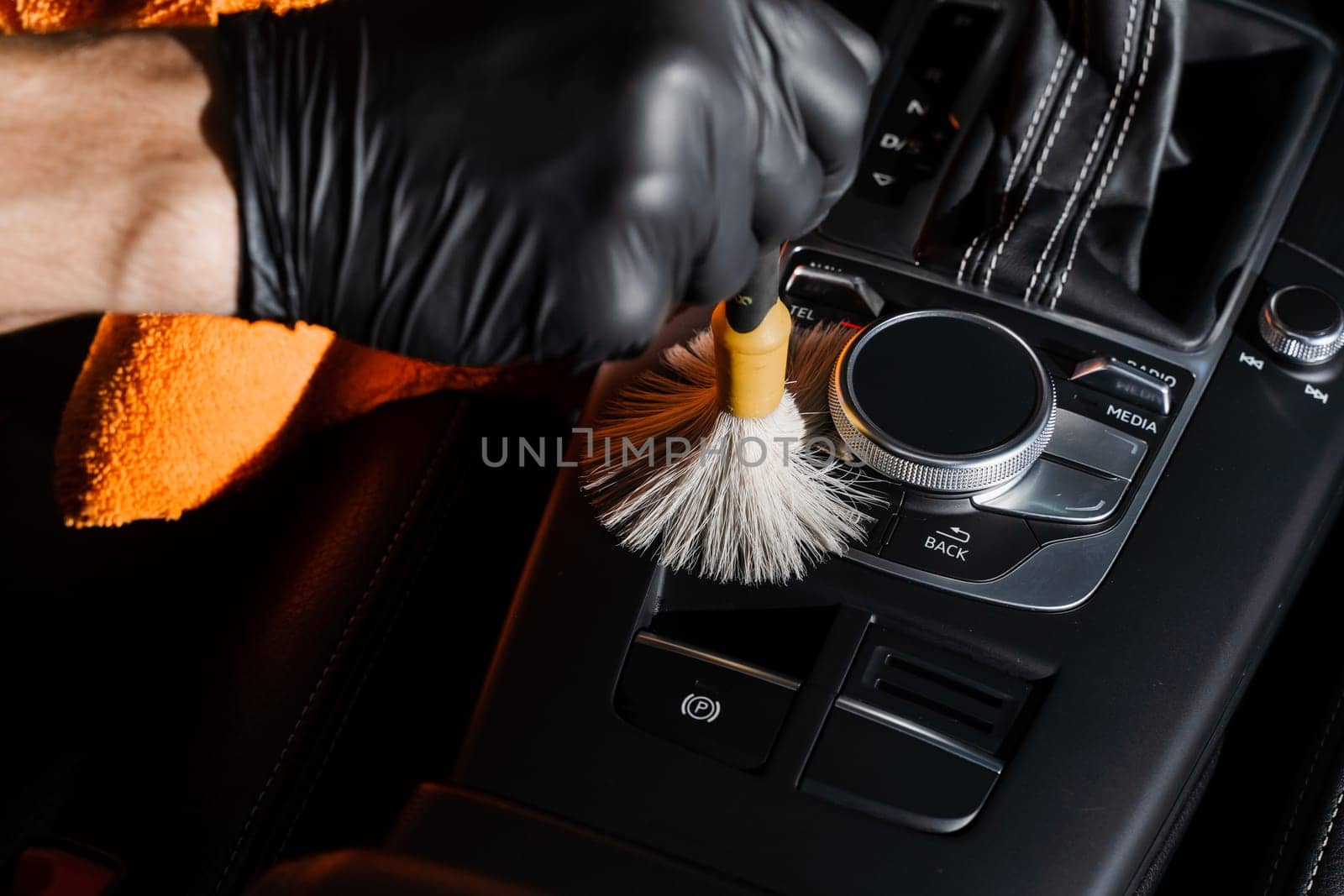 Auto detailing service. Dry cleaning with brush of gearbox and dashboard in car. Cleaning individual elements of black leather interior in auto. by Rabizo