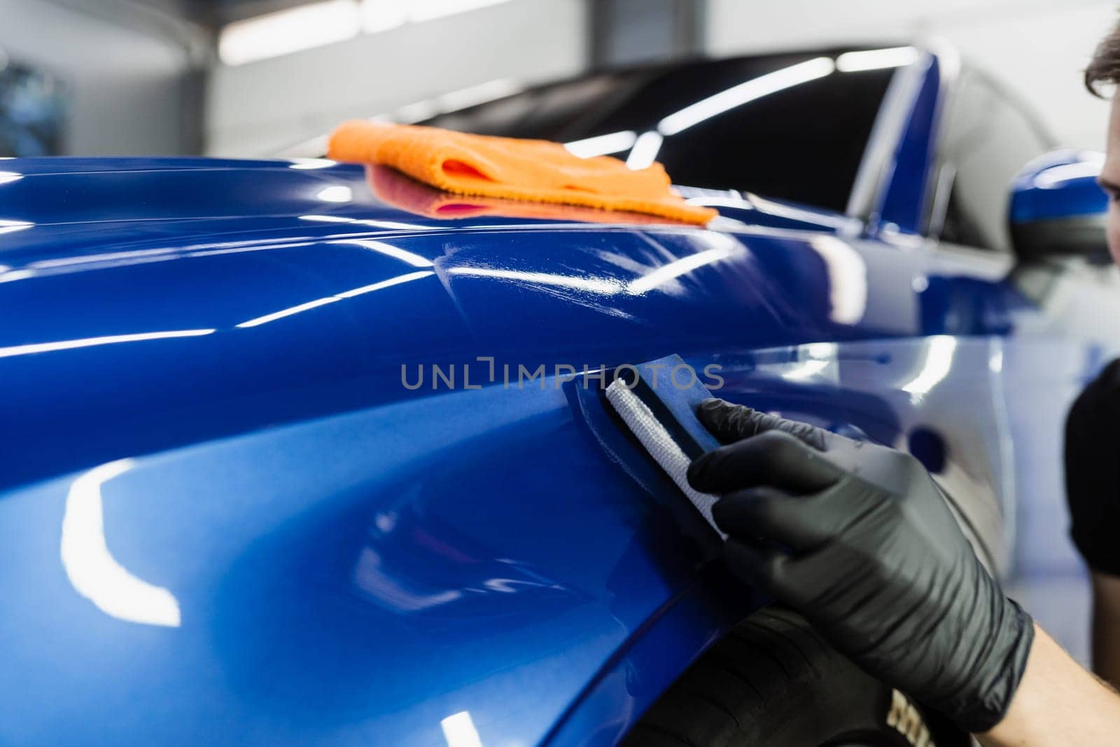 Process of applying ceramic protective coat on body car using sponge in detailing auto service. Car service worker apply ceramic coating to protect the car body from scratches. by Rabizo