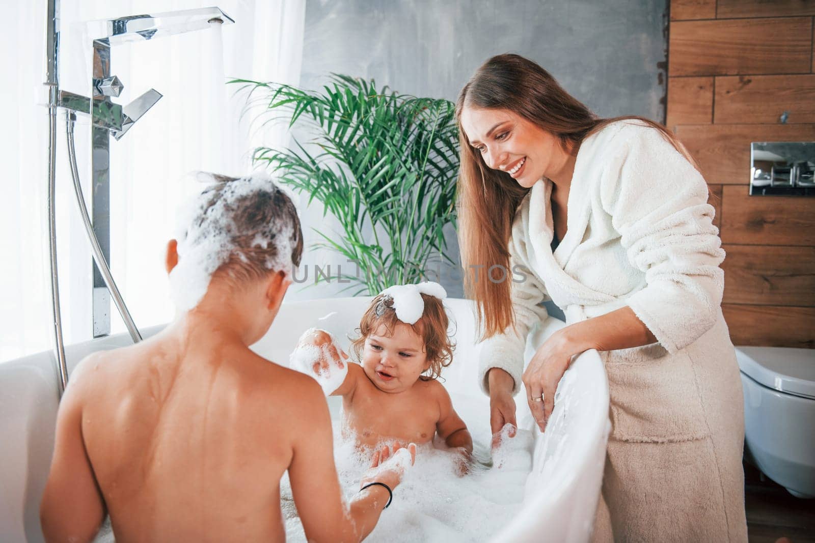 Having fun. Young mother helps her son and daughter. Two kids washing in the bath by Standret