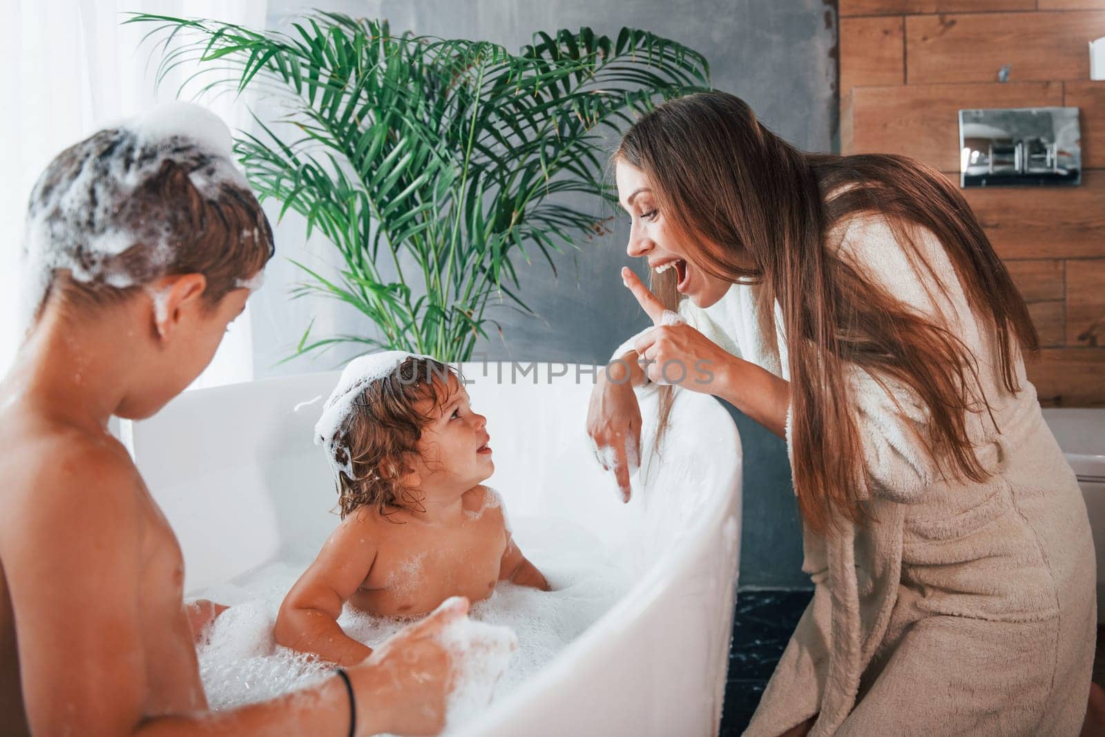 Having fun. Young mother helps her son and daughter. Two kids washing in the bath by Standret