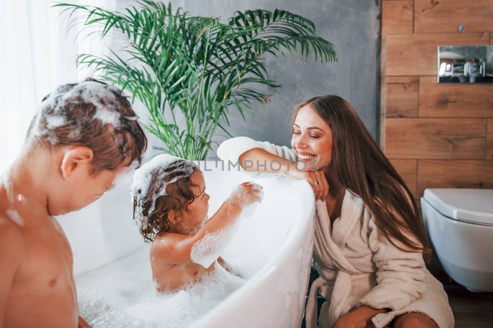 Having fun. Young mother helps her son and daughter. Two kids washing in the bath by Standret