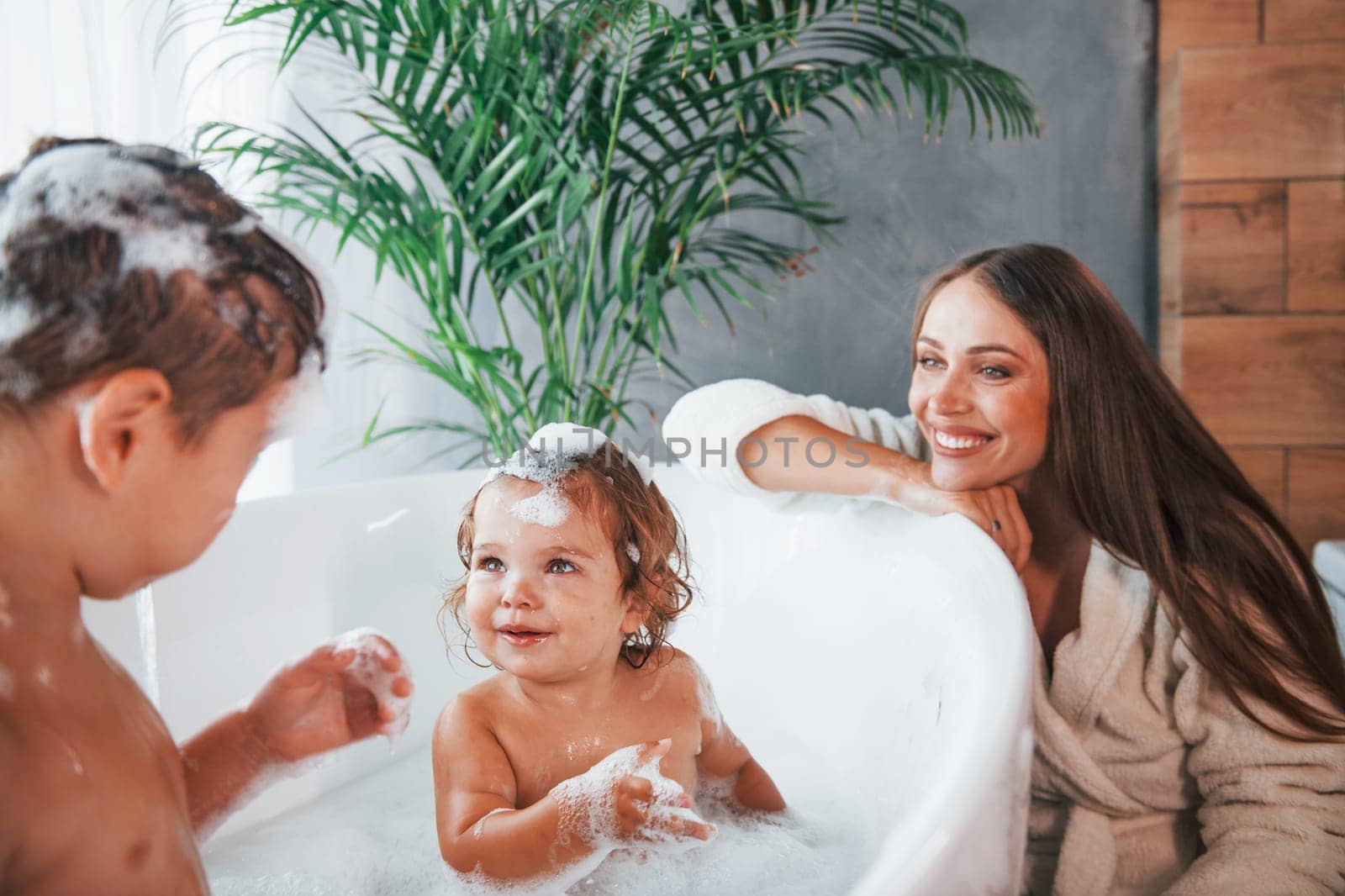 Having fun. Young mother helps her son and daughter. Two kids washing in the bath.