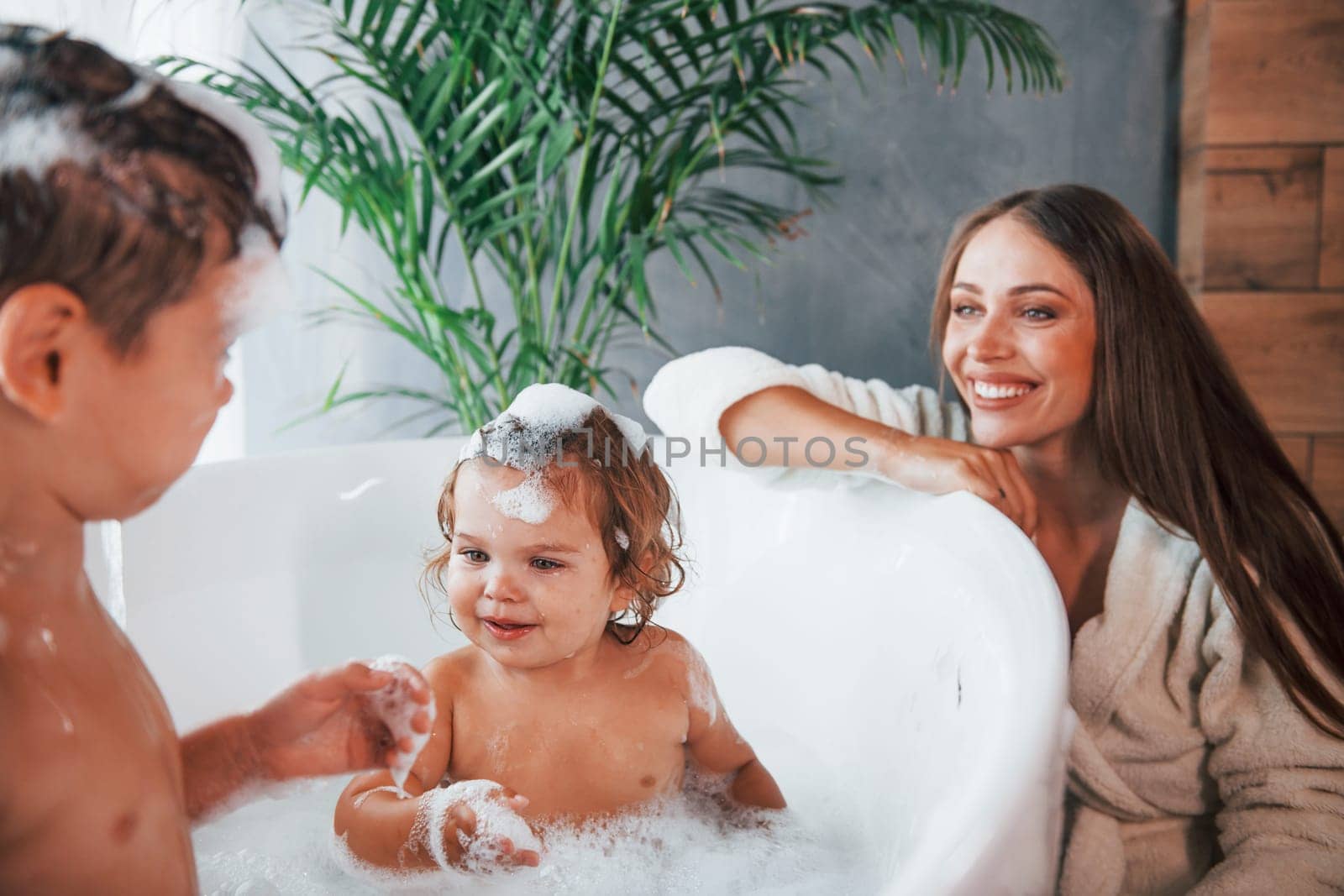 Having fun. Young mother helps her son and daughter. Two kids washing in the bath.