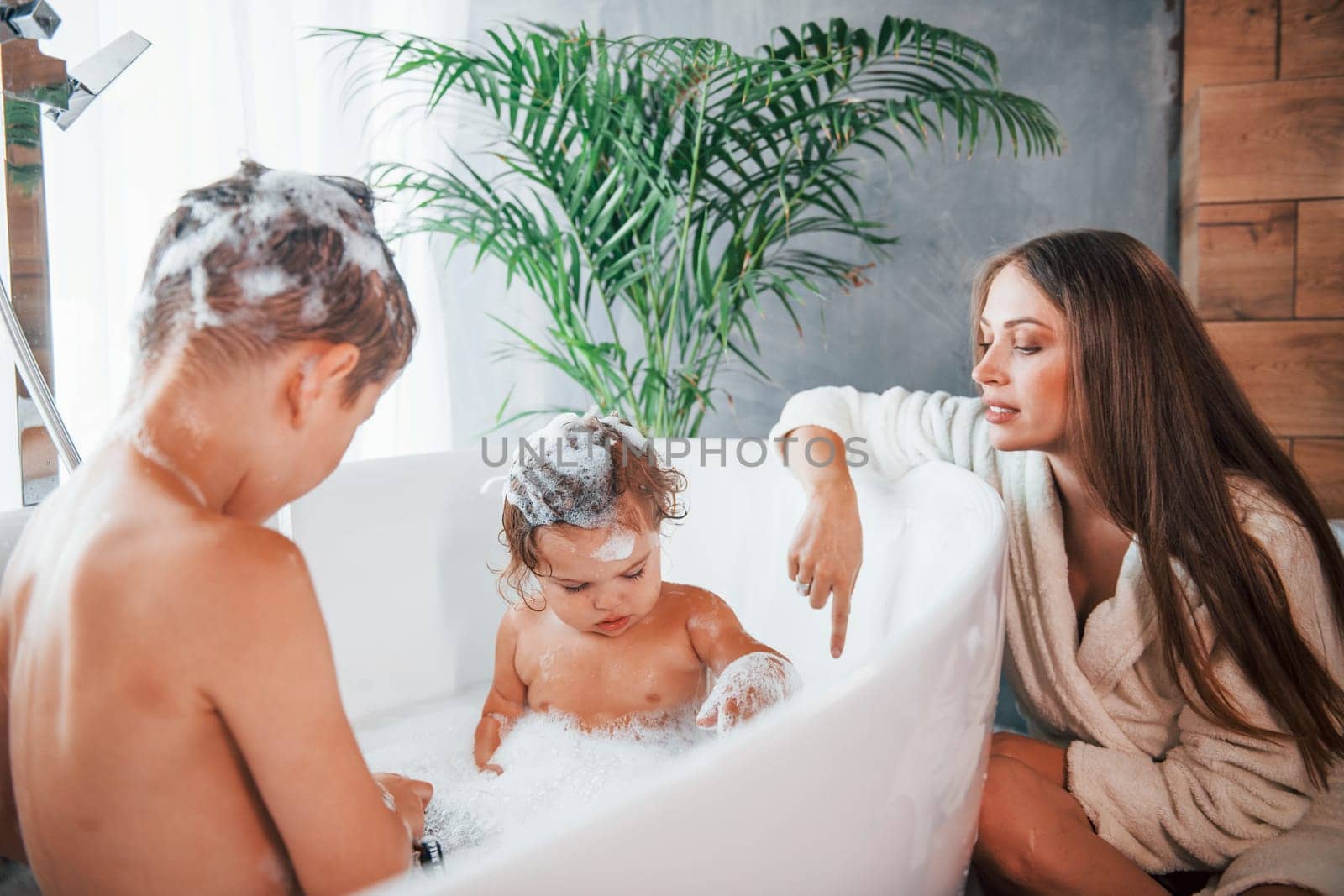 Having fun. Young mother helps her son and daughter. Two kids washing in the bath by Standret