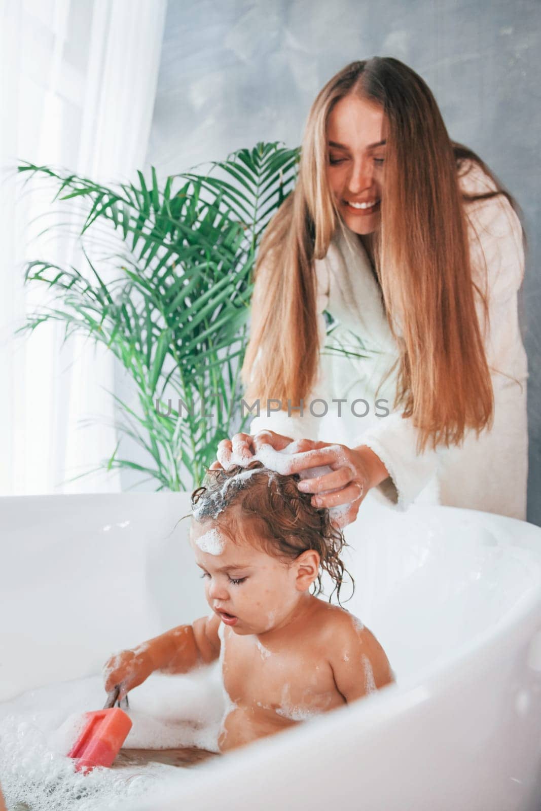 Young mother helps her daughter to wash in the bath.