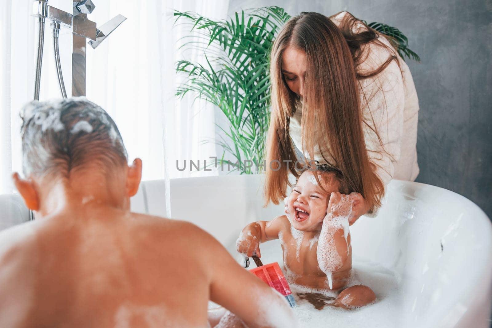 Having fun. Young mother helps her son and daughter. Two kids washing in the bath by Standret