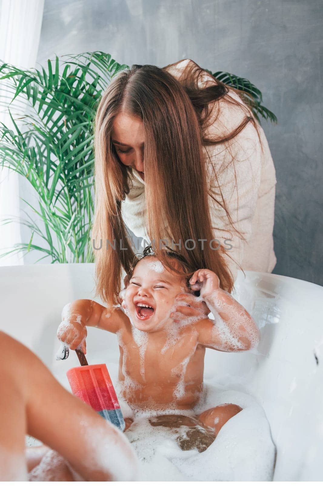 Having fun. Young mother helps her son and daughter. Two kids washing in the bath.