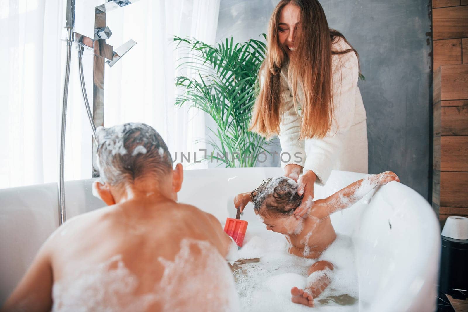 Having fun. Young mother helps her son and daughter. Two kids washing in the bath.