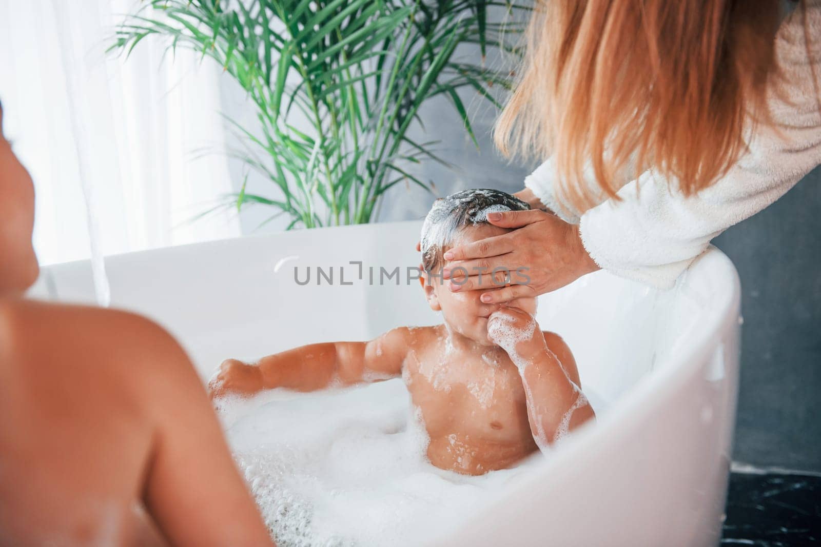 Having fun. Young mother helps her son and daughter. Two kids washing in the bath.