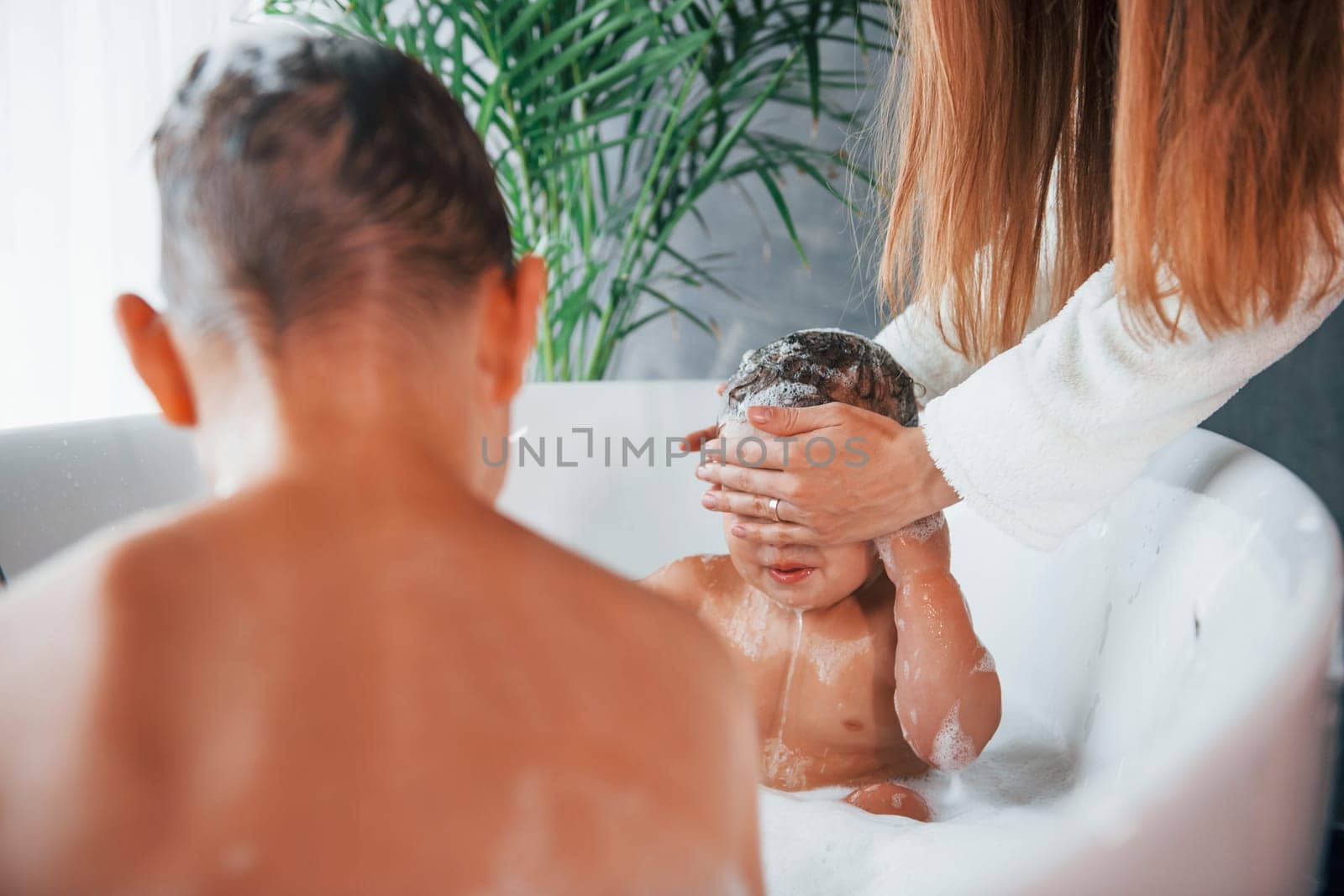 Having fun. Young mother helps her son and daughter. Two kids washing in the bath.