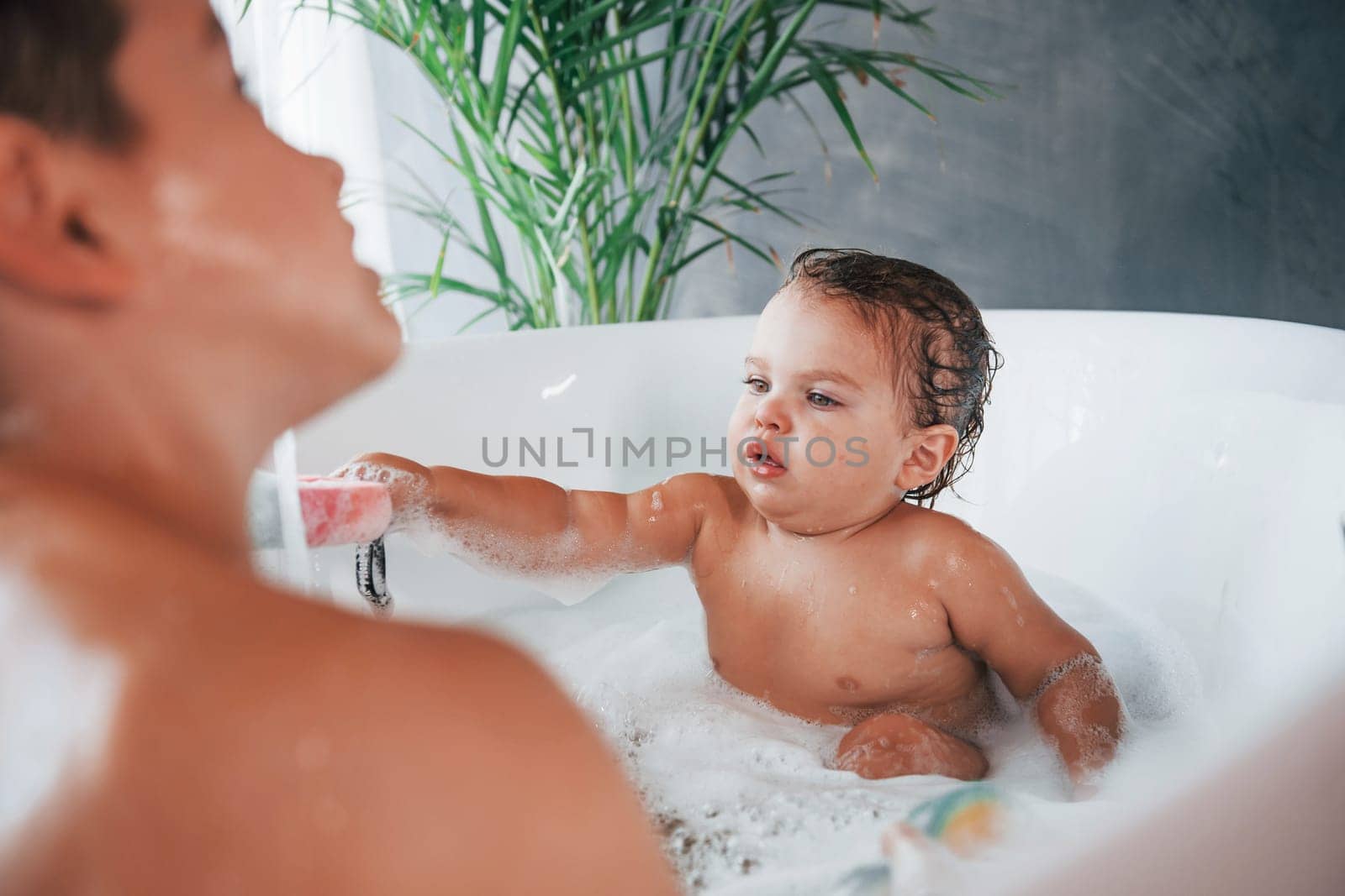 Two kids having fun and washing themselves in the bath at home.