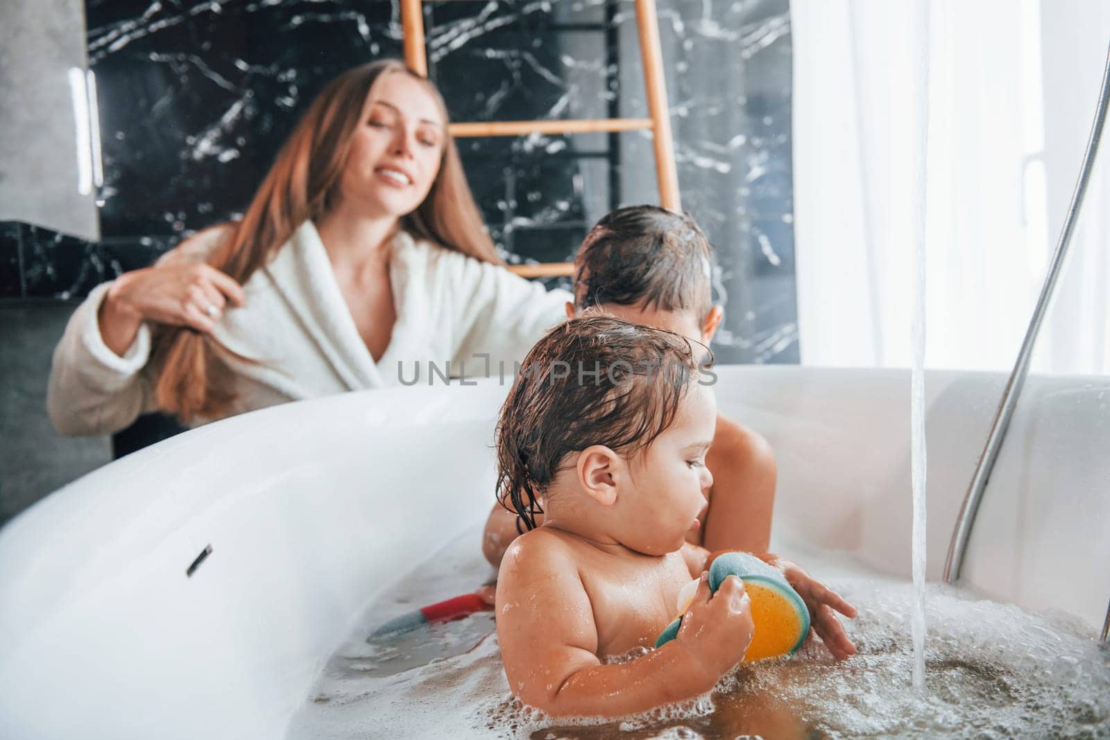 Having fun. Young mother helps her son and daughter. Two kids washing in the bath.
