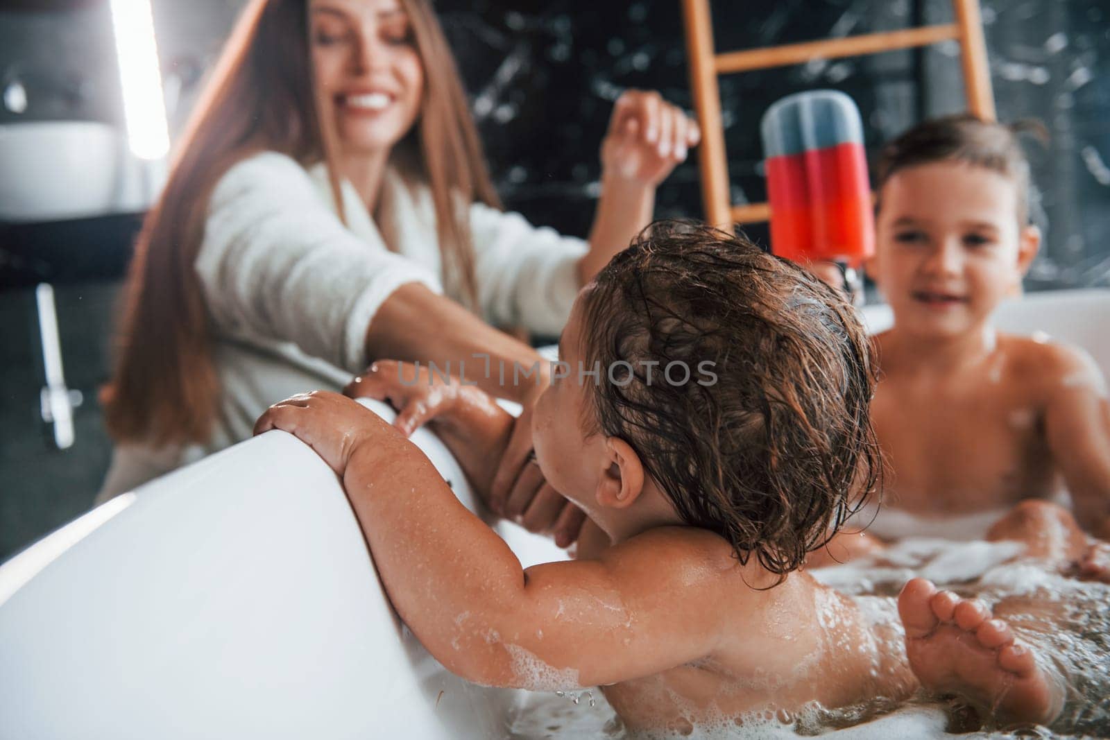 Young mother helps her son and daughter. Two kids washing in the bath by Standret